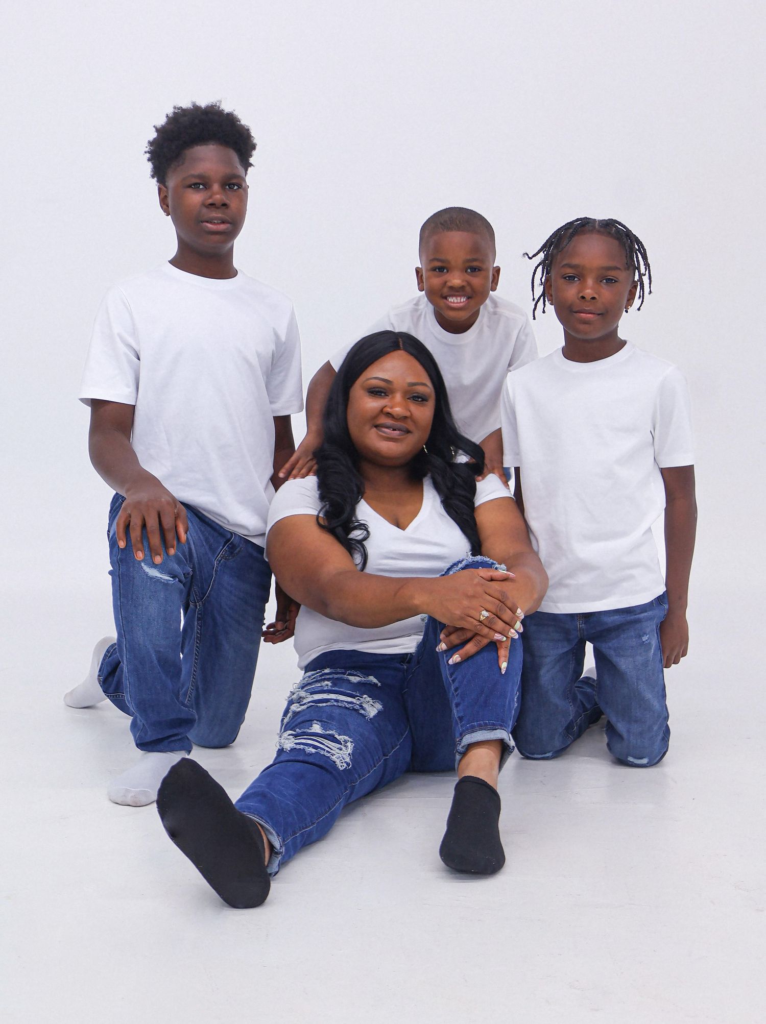 A mother poses with her three sons, all wearing white tees and jeans, in a bright studio setting.
