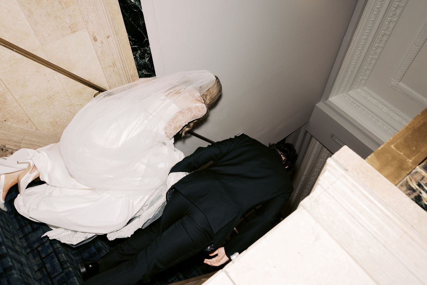 Person in white veil and black outfit crouched in a marble corner, artistic fashion photography.