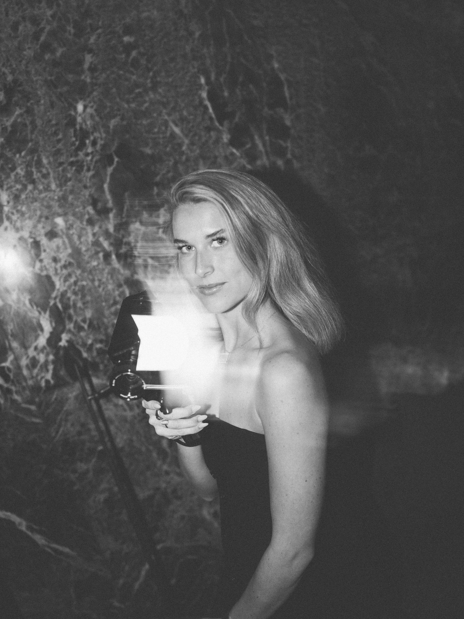 Artistic black and white portrait of someone holding a glowing light source against a dark textured background.
