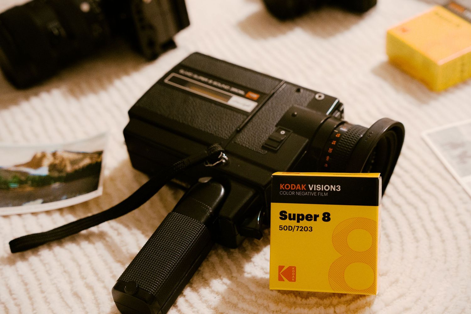 Kodak Vision3 Super 8 500T film cartridge beside a vintage Super 8 movie camera on a white surface.