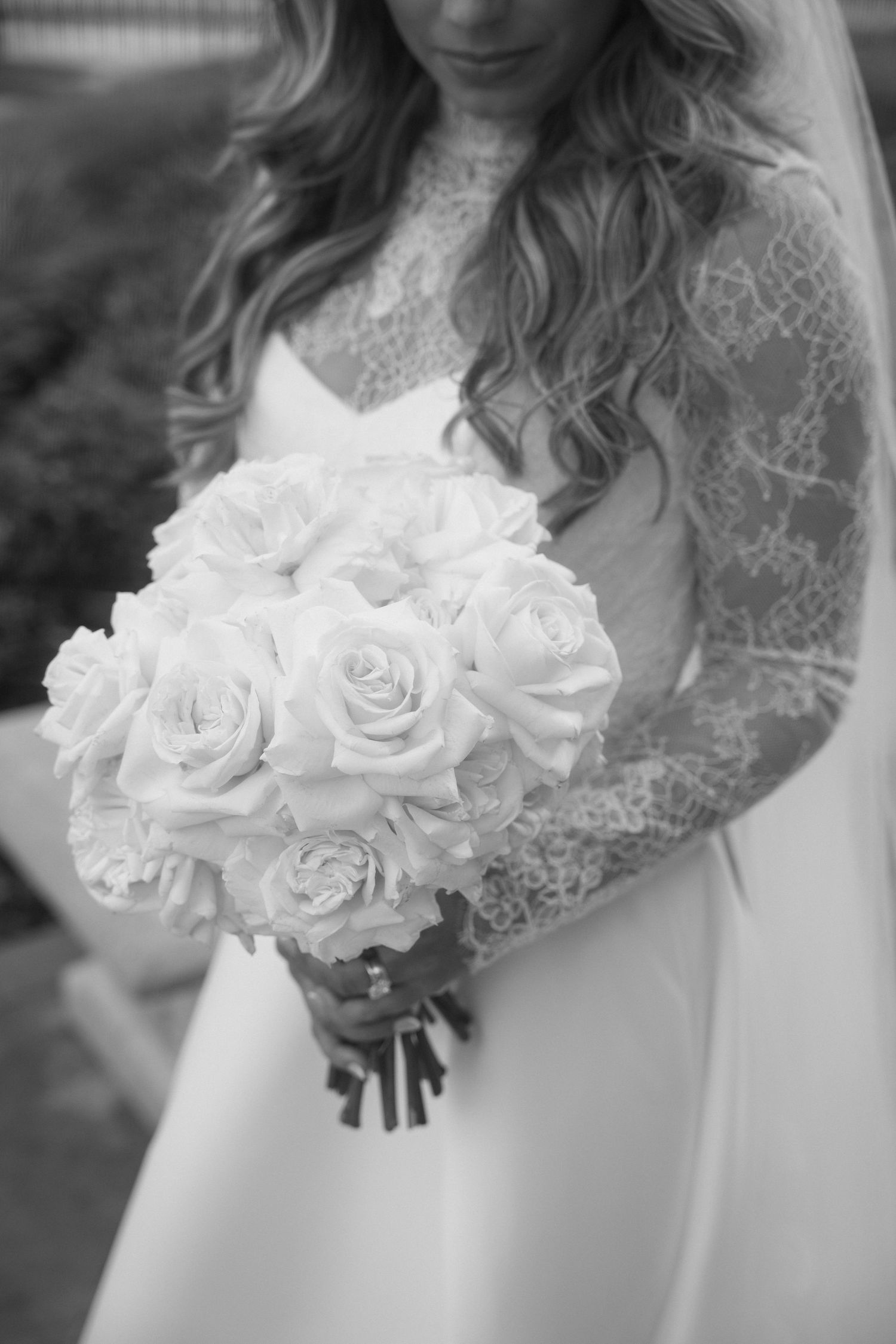 Black and white photo of a bride in lace gown holding a round bouquet of white roses on her wedding day.