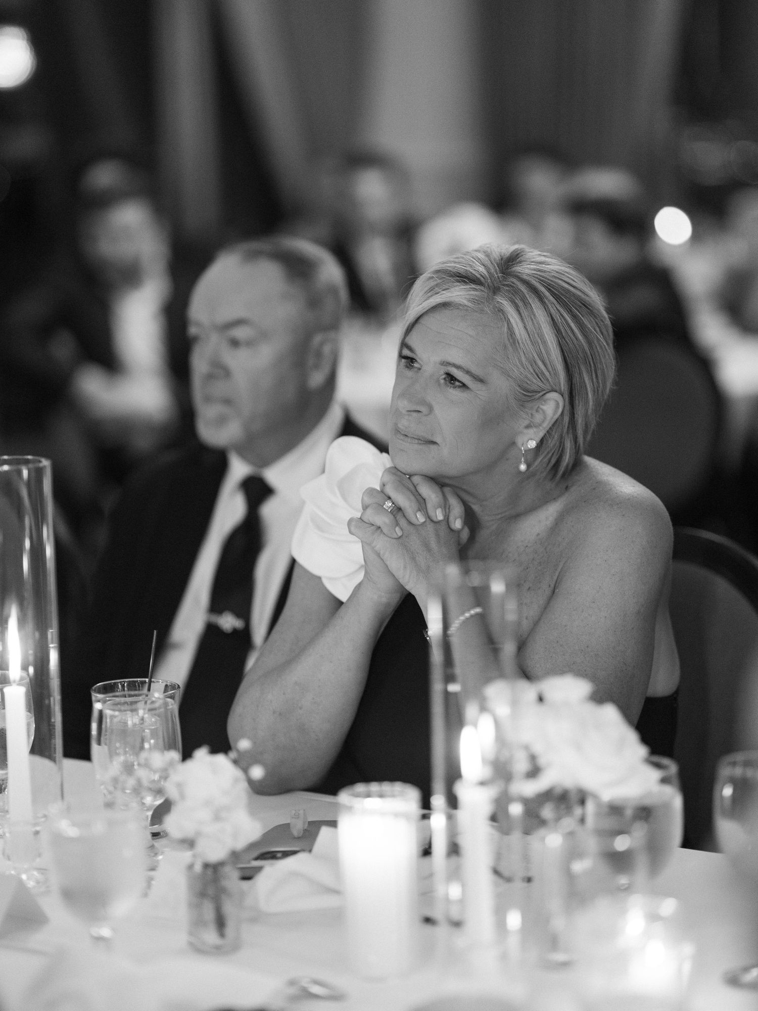 Black and white photo of emotional woman dabbing tears with tissue at elegant wedding reception dinner.