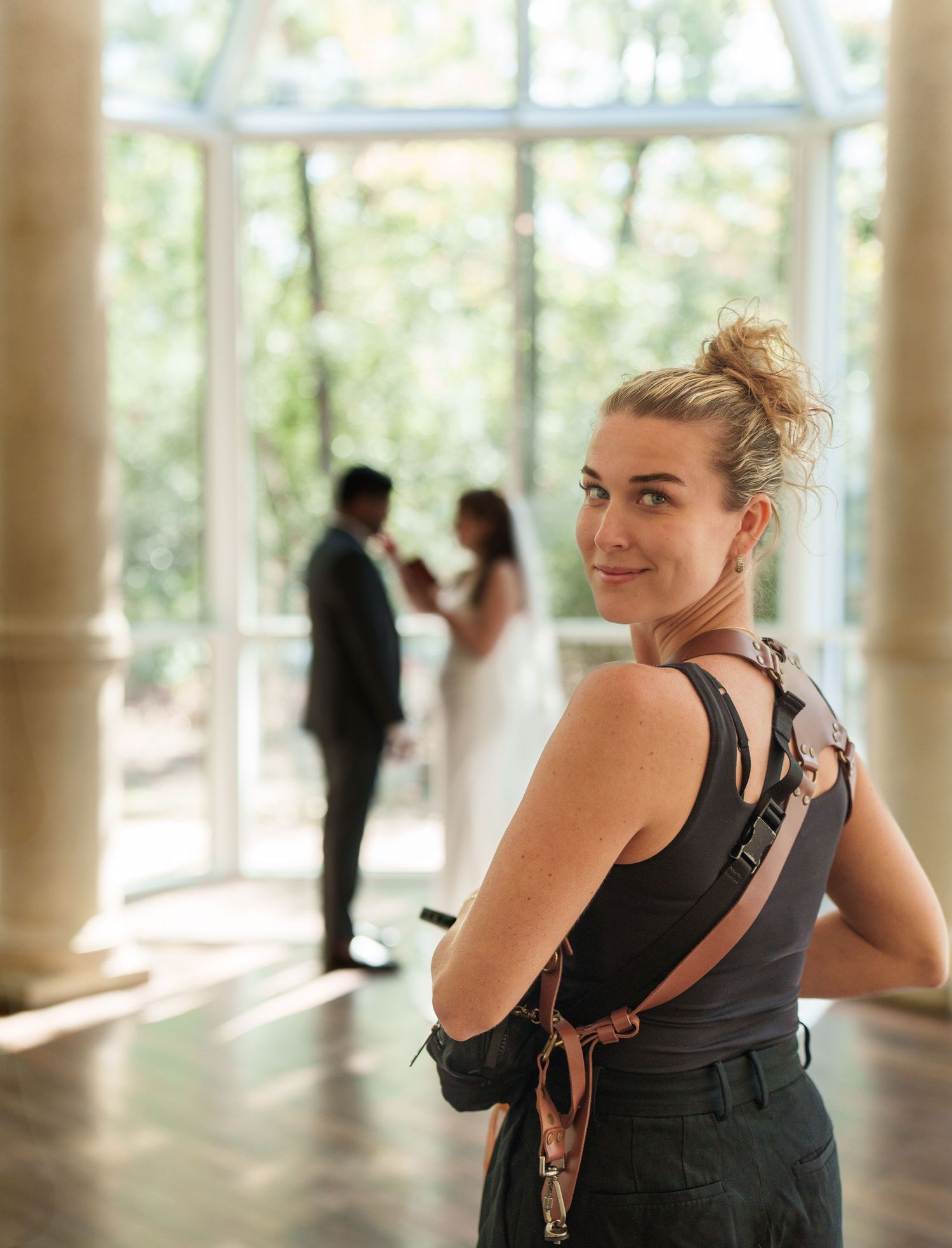 A person in a black tank top smiles while standing in a bright indoor space with columns.