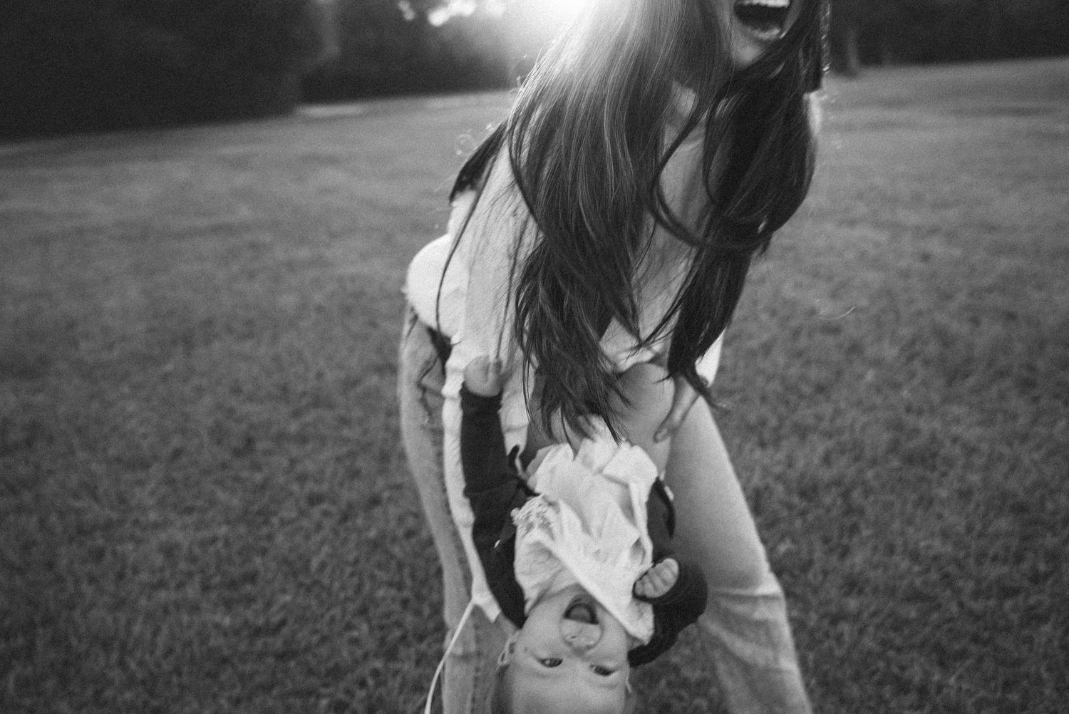 Black and white photo of someone laughing joyfully outdoors in a grassy field wearing a light colored dress.