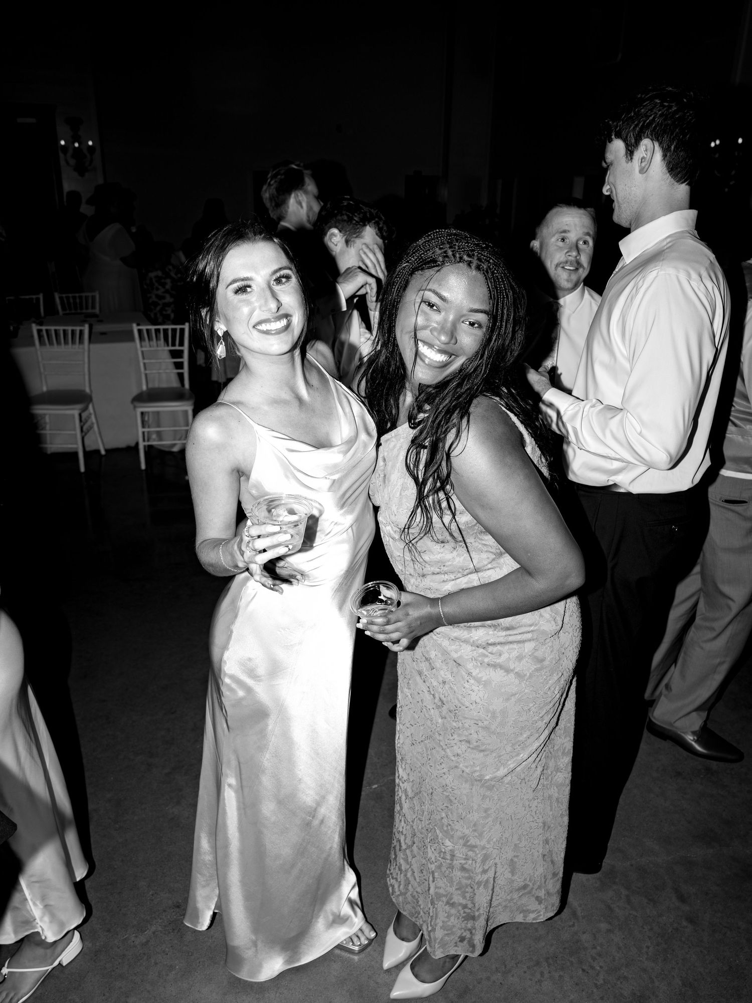 Two women smile and pose together at a formal event, wearing elegant gowns in a black and white photo.