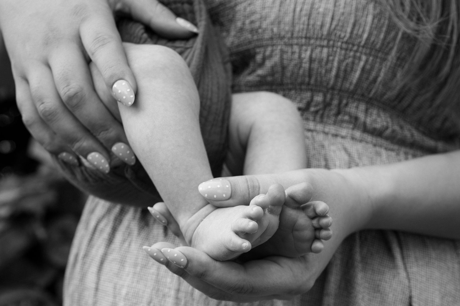 Black and white photo of a mother cradling her newborn baby's tiny feet in her hands.