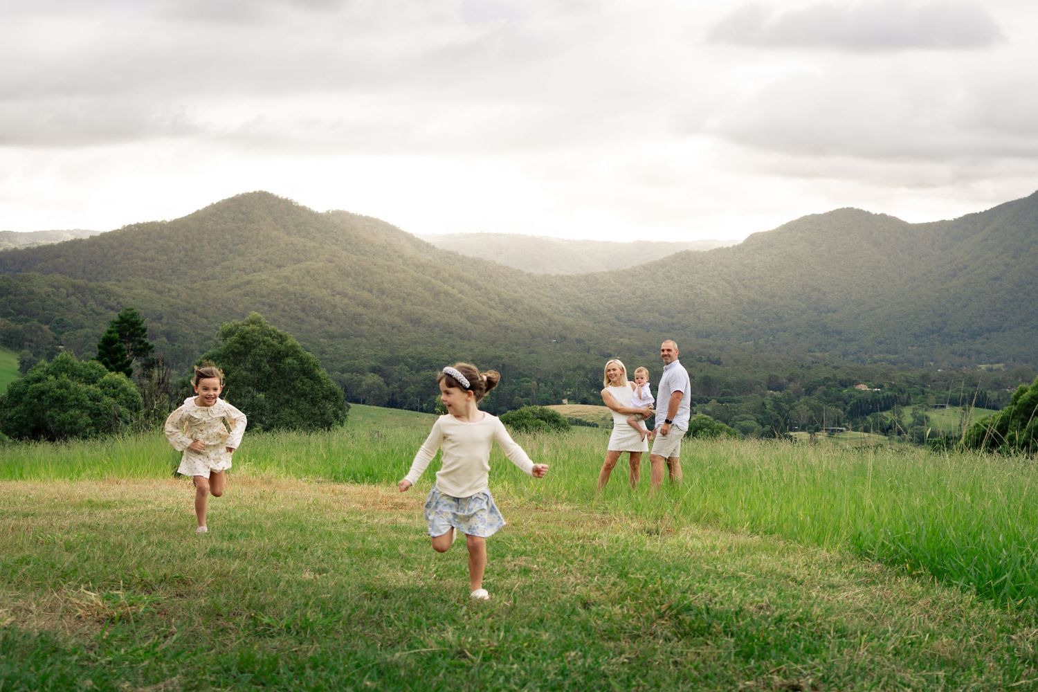 Family with two children playing on a green hillside meadow with lush mountain ranges in the background.