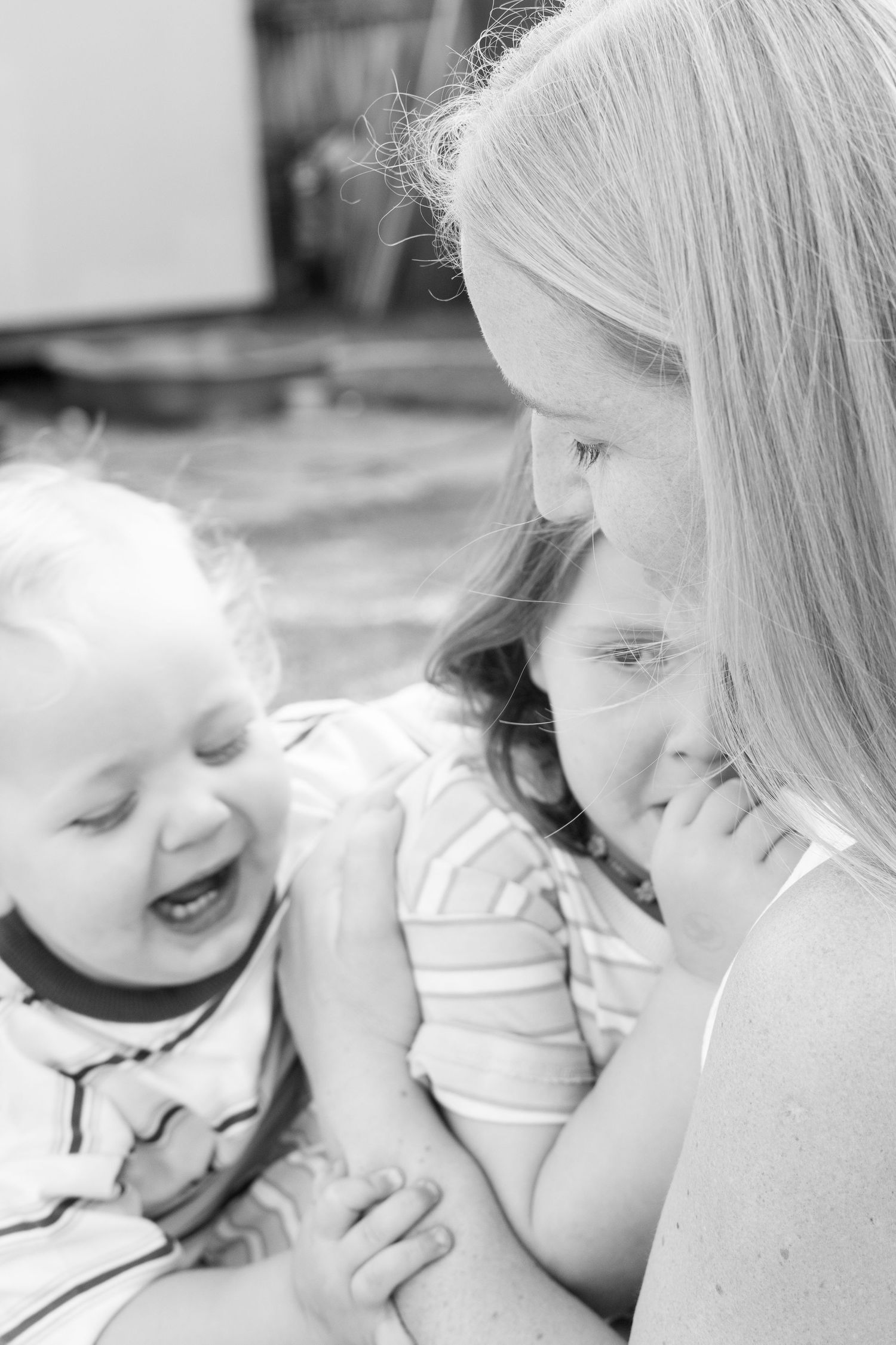 Black and white photo of a smiling mother holding two young laughing children in a warm, candid family moment.