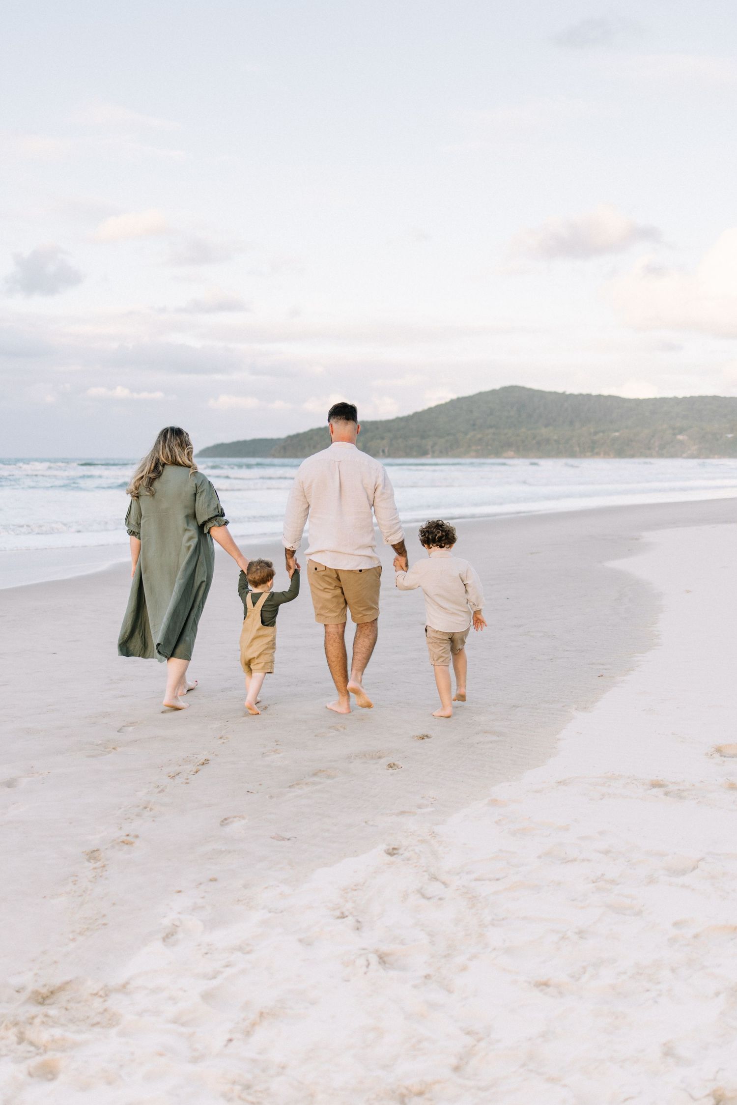 A family of four walks hand in hand along a serene beach at dusk.