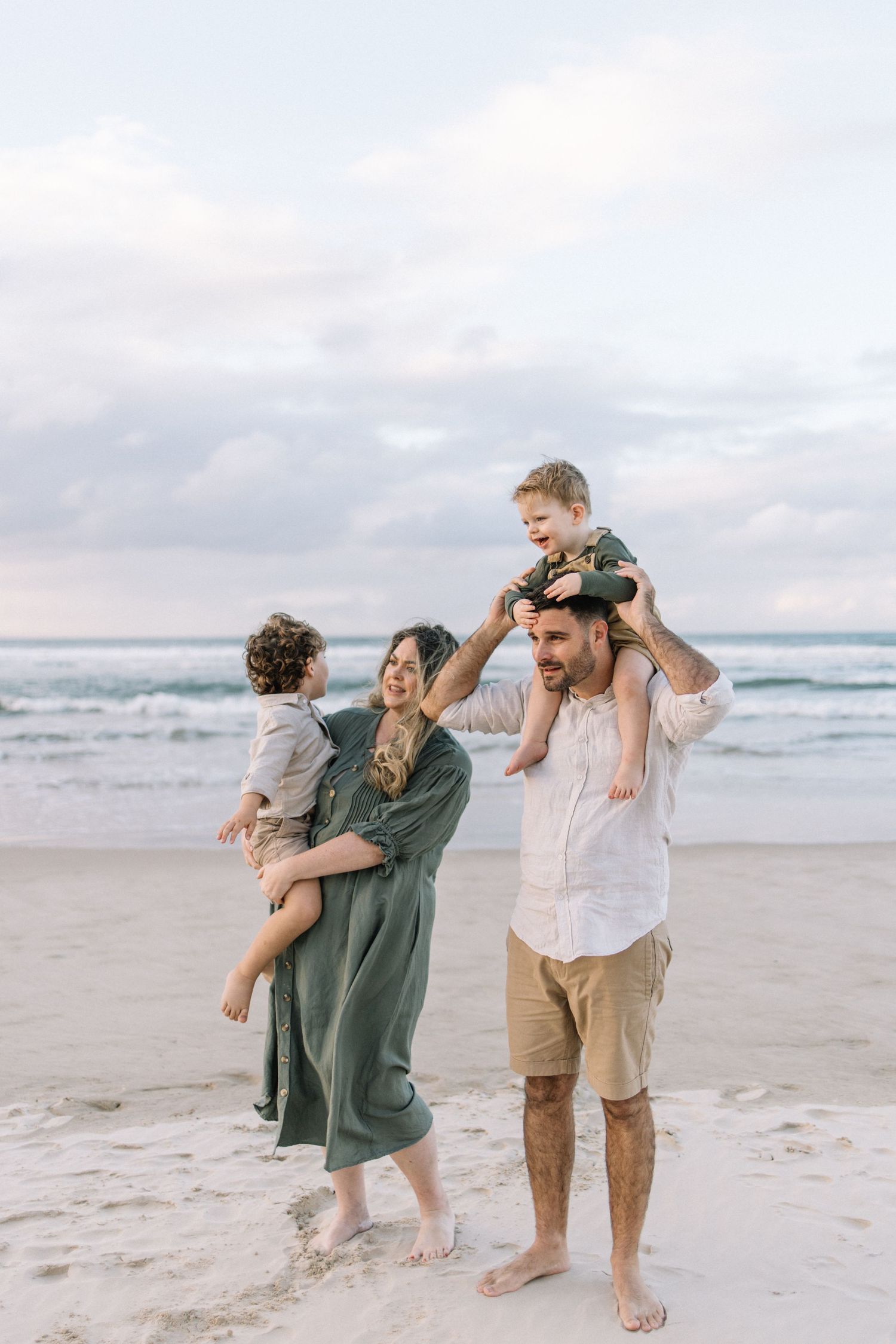 A happy family with two young children plays on a beach at sunset, mother in green dress.