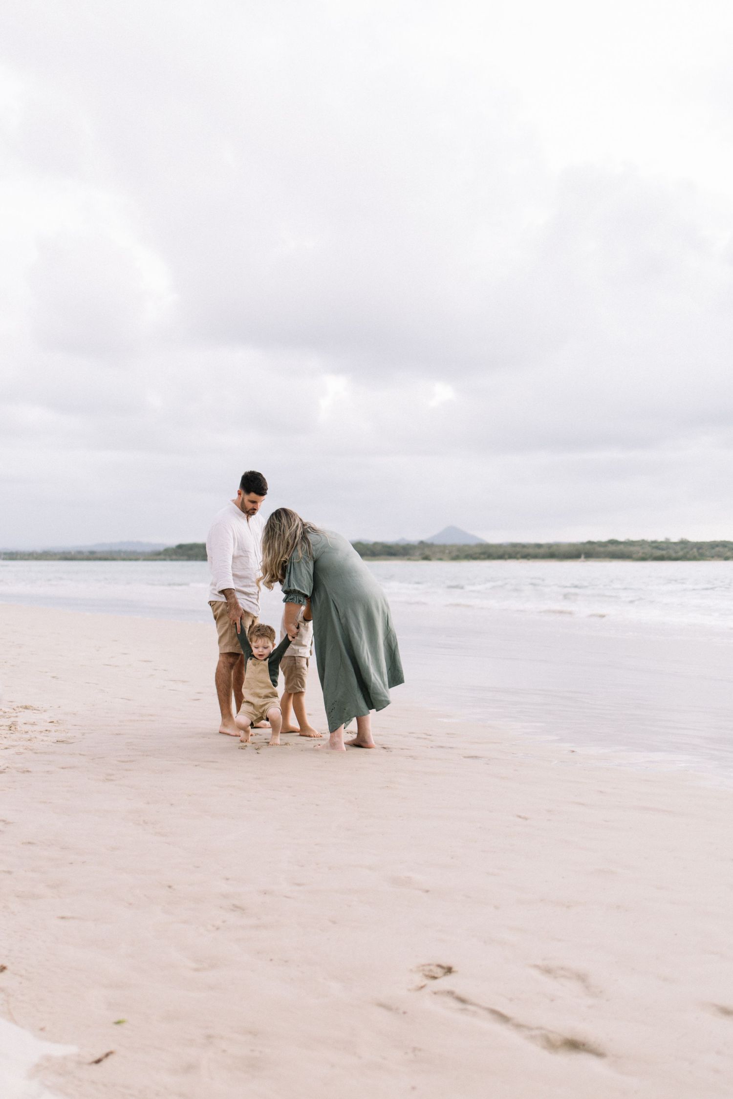 A family of four enjoys a peaceful walk together along a sandy beach on a cloudy day.