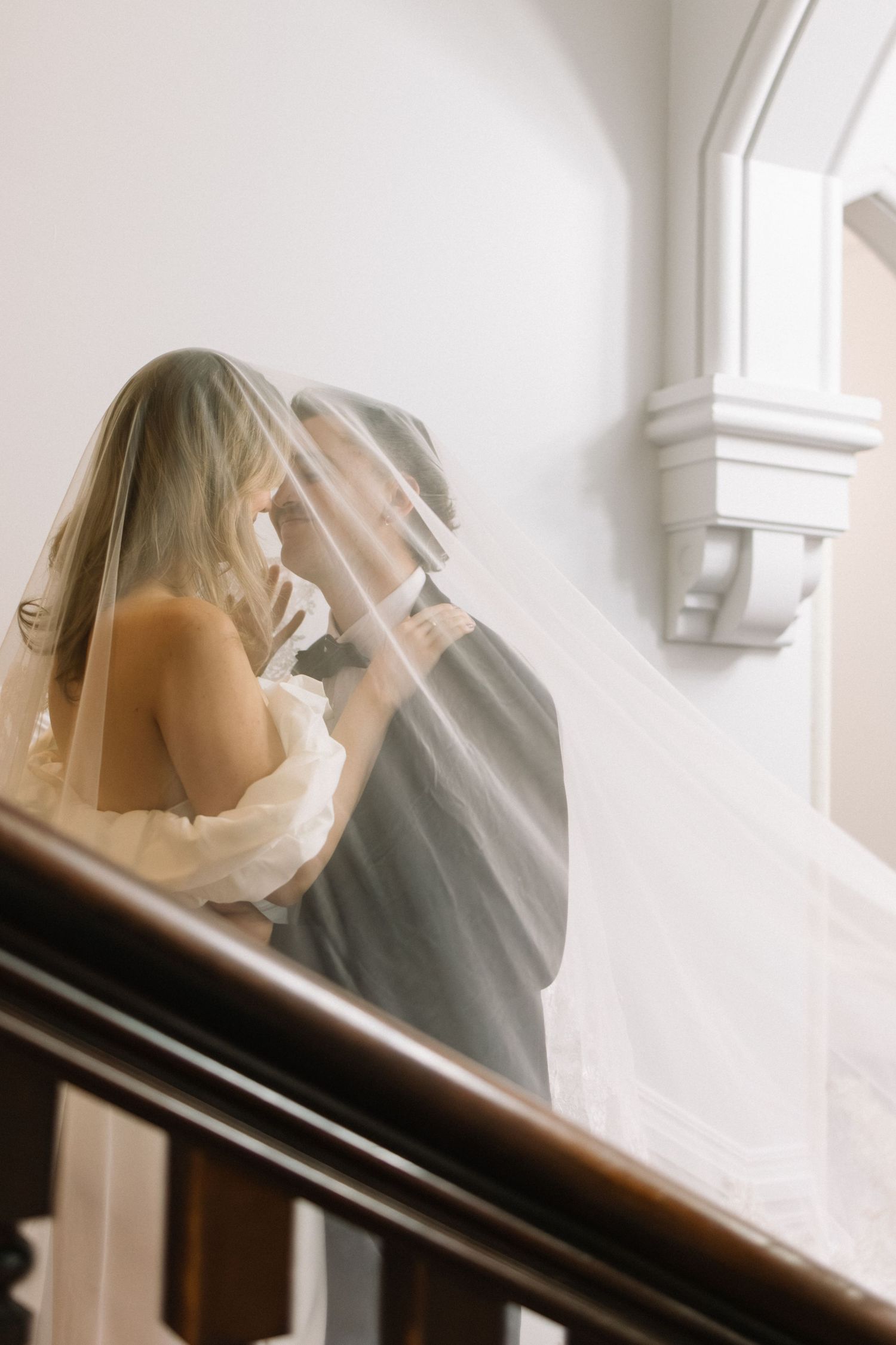 Bride and groom sharing an intimate moment under a veil on an elegant staircase.