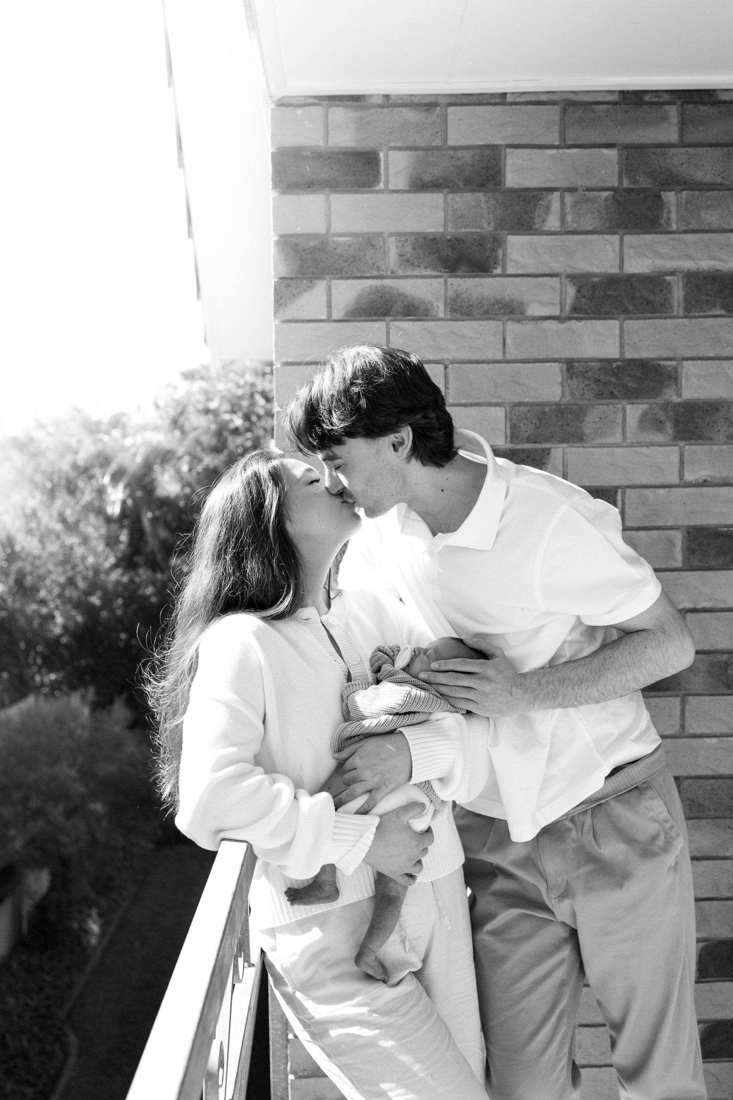 Black and white photo of a romantic couple kissing on a balcony beside a brick wall.
Family photography