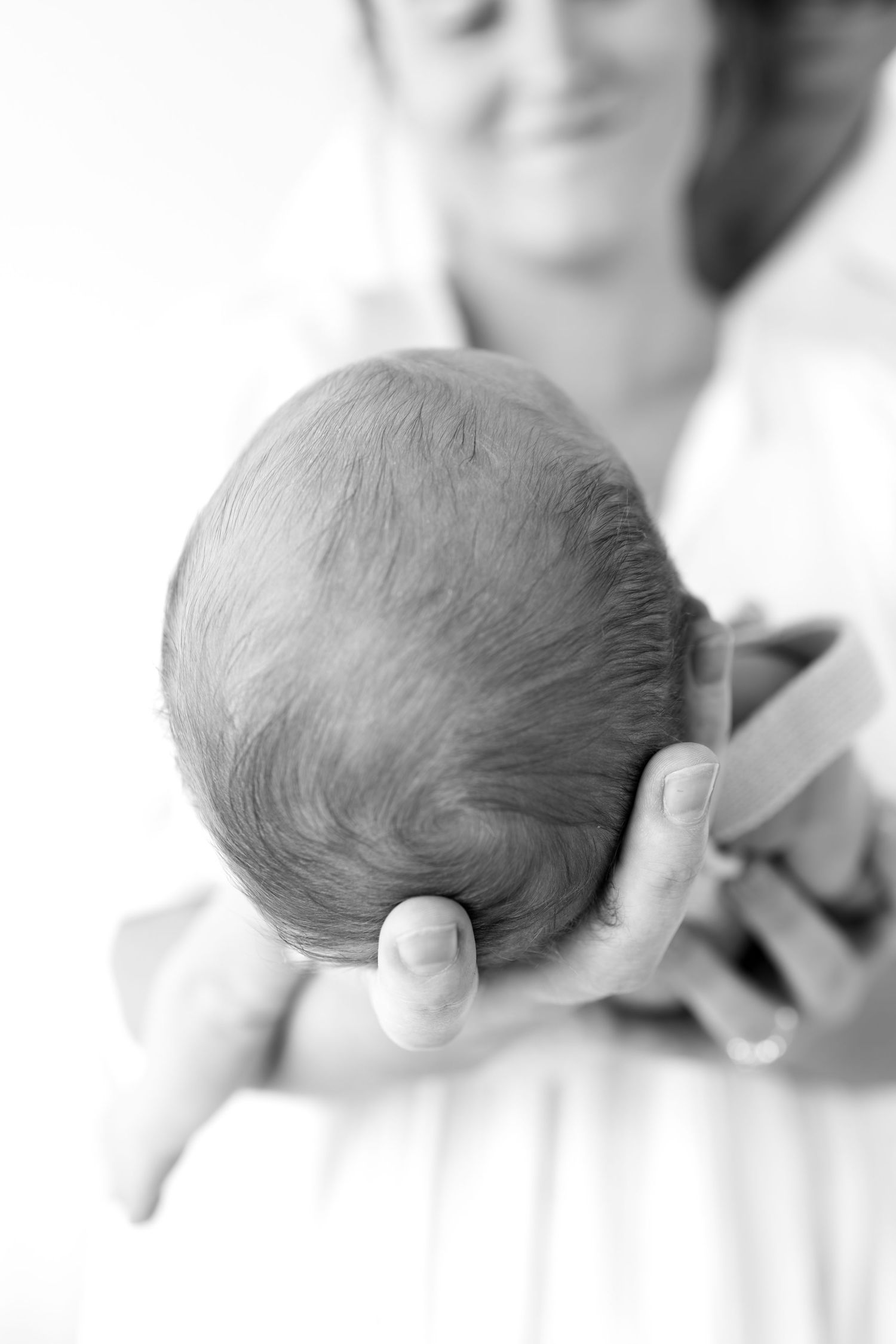 Black and white photo of smiling mother holding newborn baby showing back of head.
