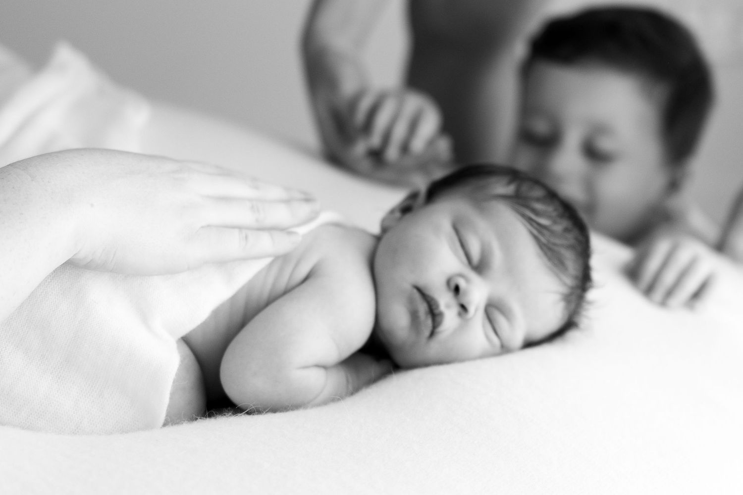 Black and white newborn photo with sleeping baby and older sibling looking on tenderly.