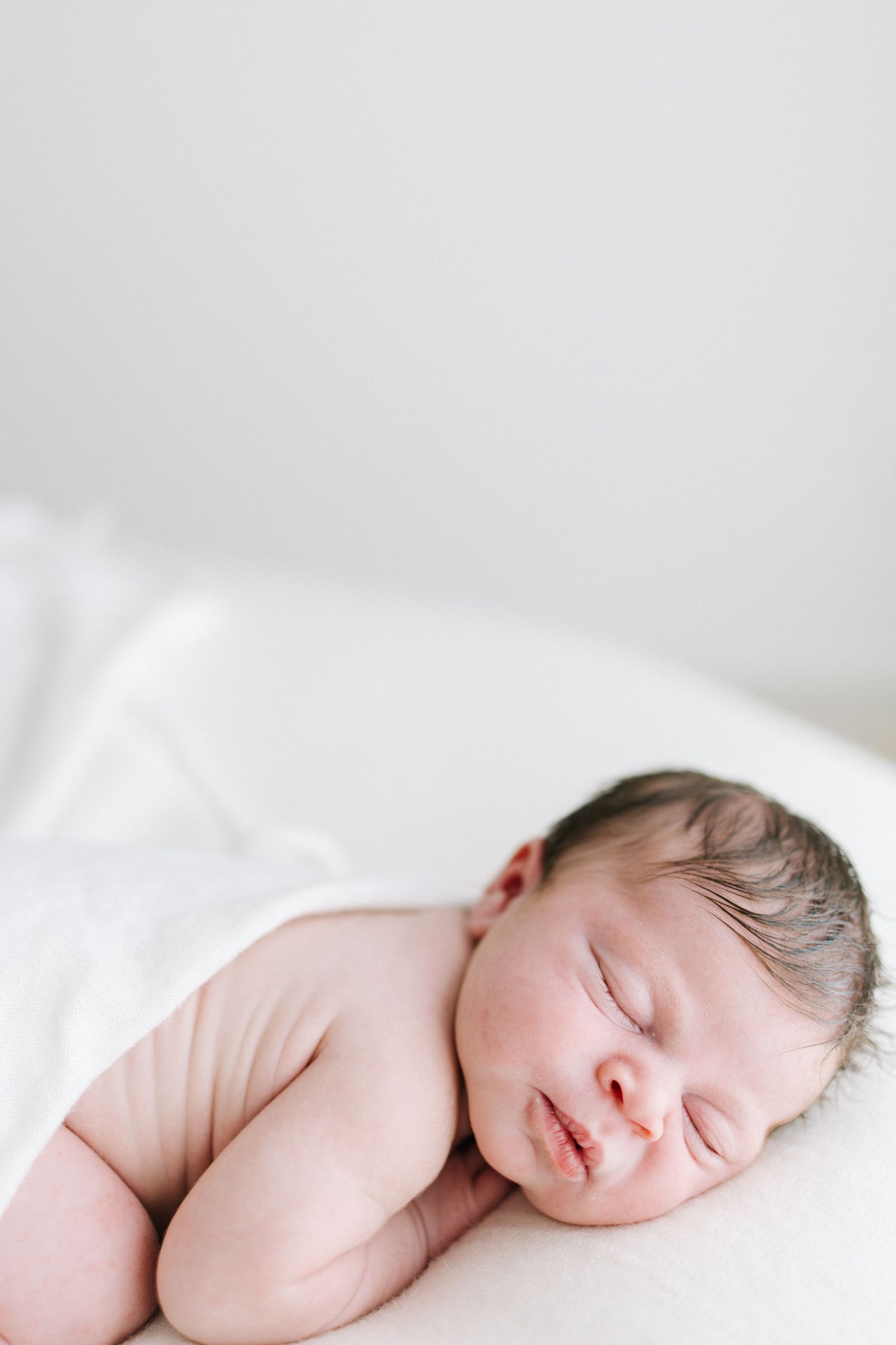 Peaceful newborn baby sleeping on white blanket with dark hair and soft skin in serene portrait photo.