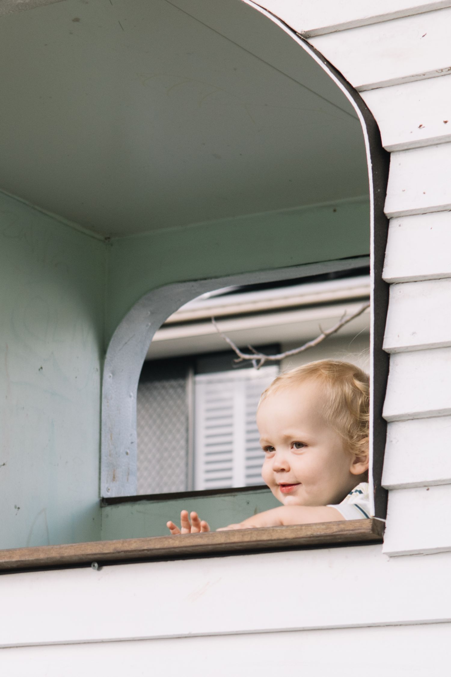 Curious toddler peering out of an open trailer window, smiling with tiny hands gripping the ledge.