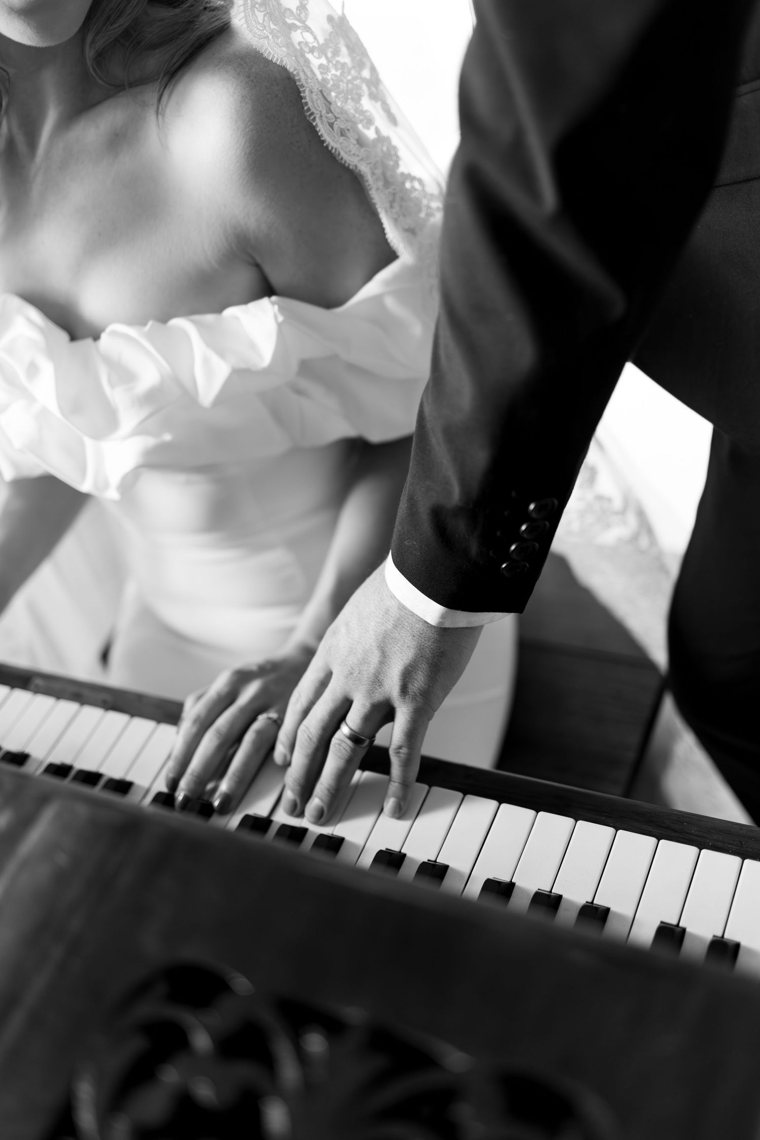Black and white photo of bride and groom playing piano together on their wedding day.