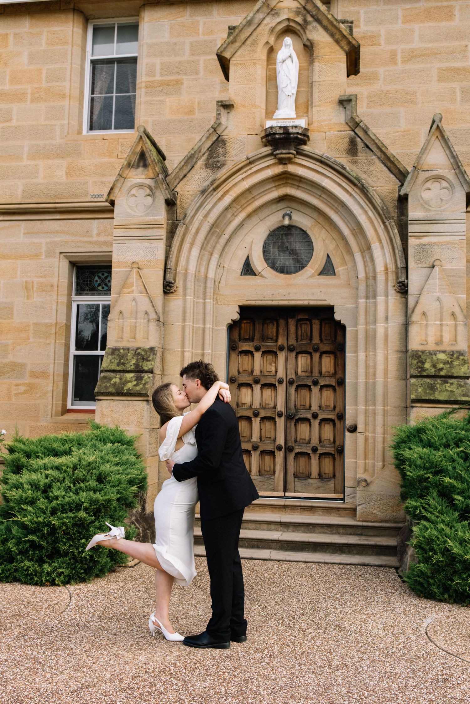 Bride and groom share a romantic kiss outside a Gothic stone church entrance with arched wooden doors.
Brisbane elopement