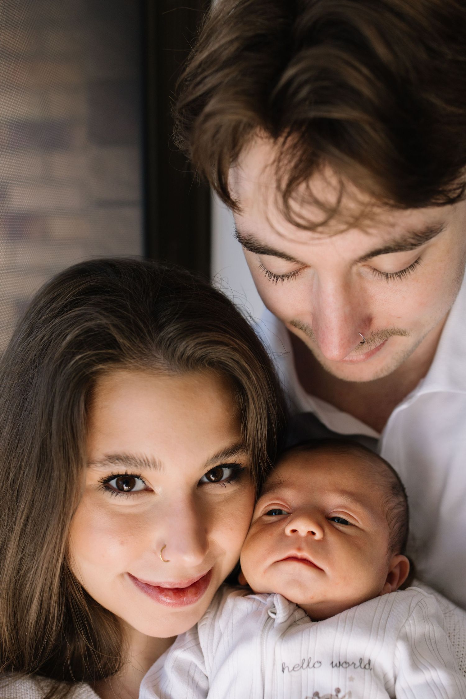 Young couple smiling with their newborn baby wearing a white hello world onesie.