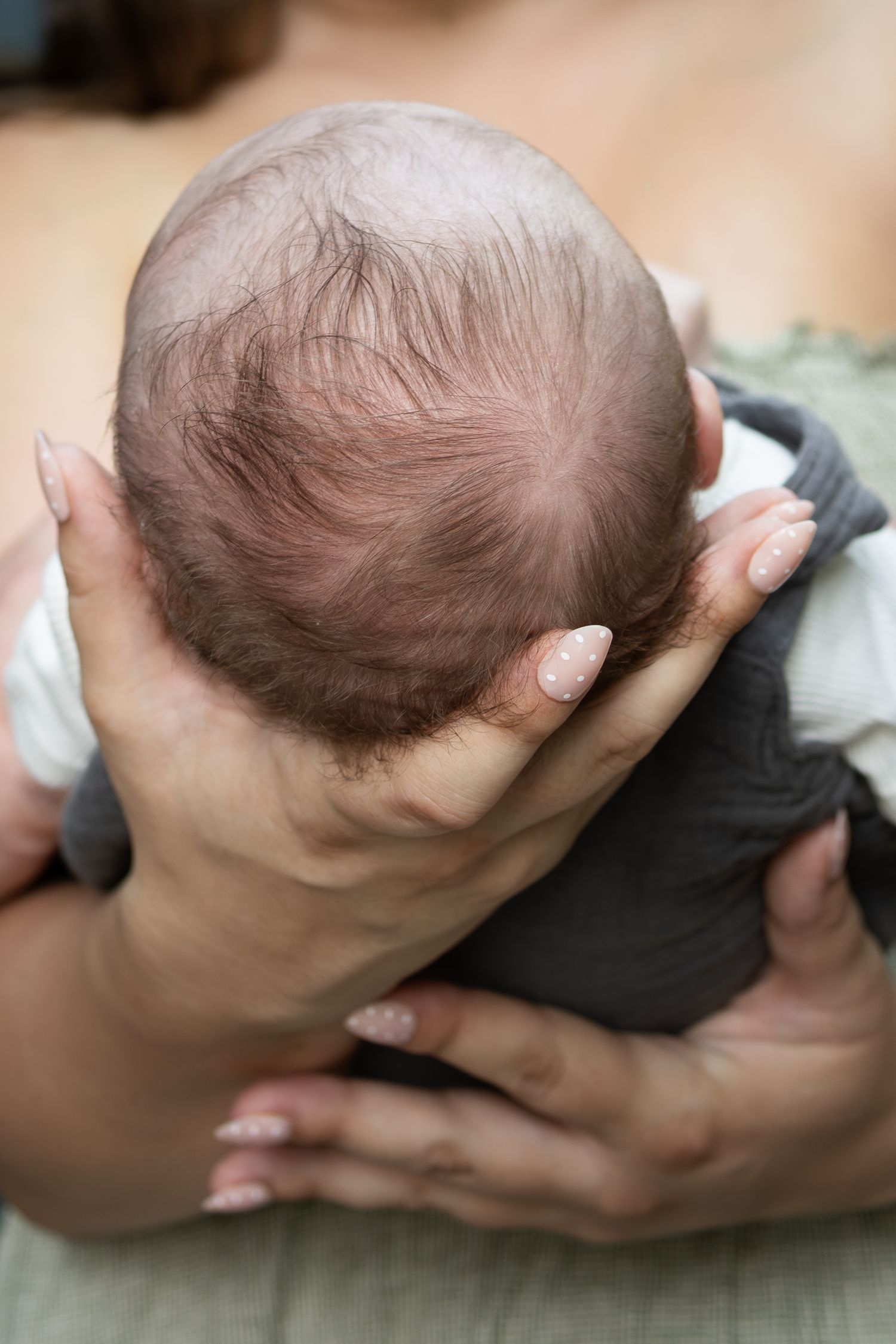 Close-up of a newborn baby's head cradled in a mother's hands, showing delicate hair and gentle support.
