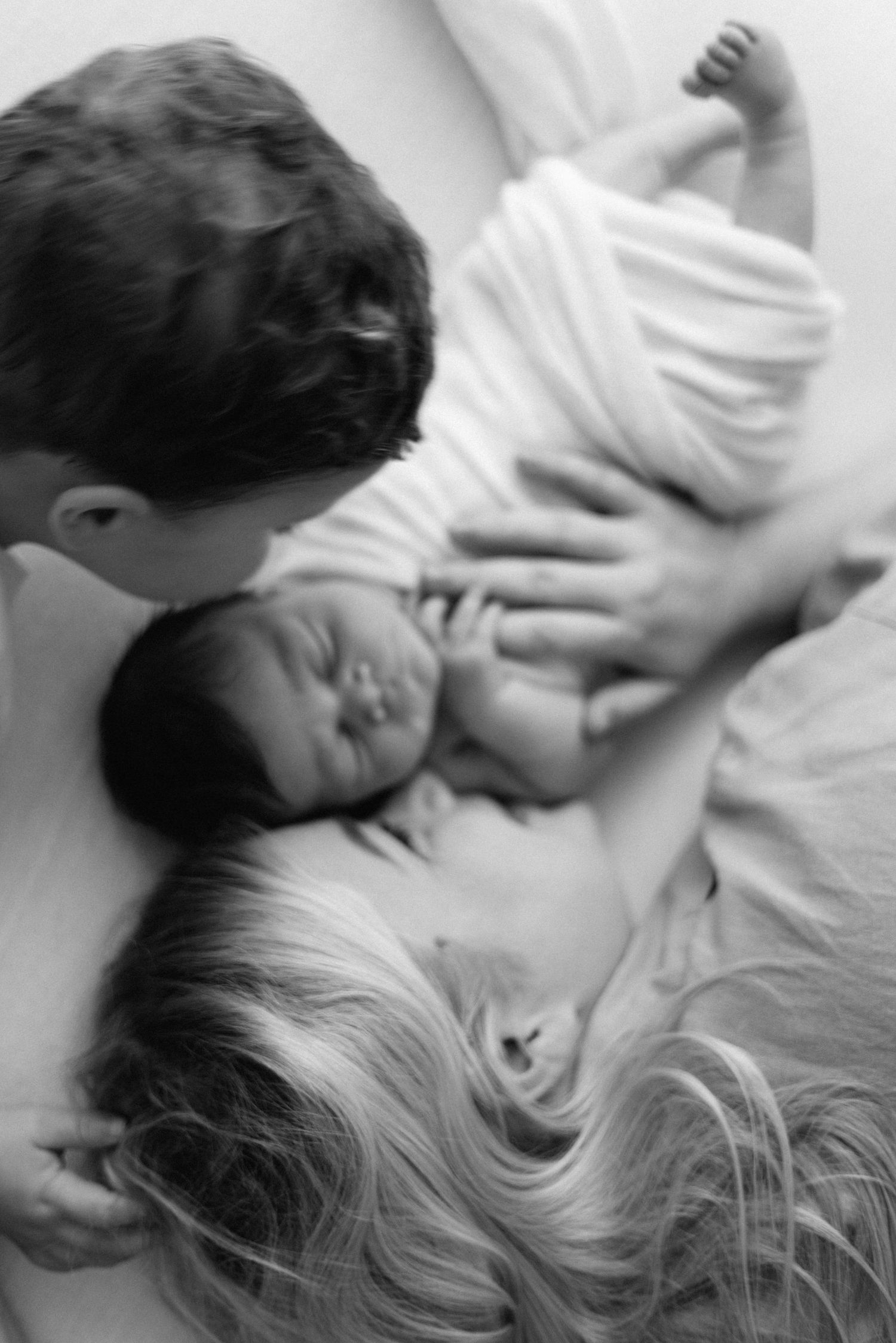 Black and white photo of parents lovingly gazing at their sleeping newborn baby.