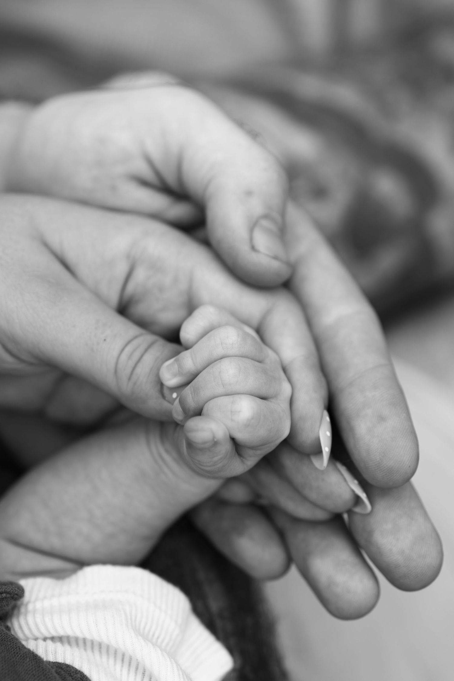 Black and white photo of a newborn baby's tiny hand gripping an adult's finger in a tender moment.
