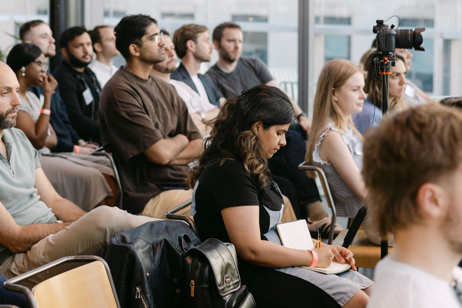 Diverse group of professionals attentively listening at a seminar or conference, seated in rows with notebooks.