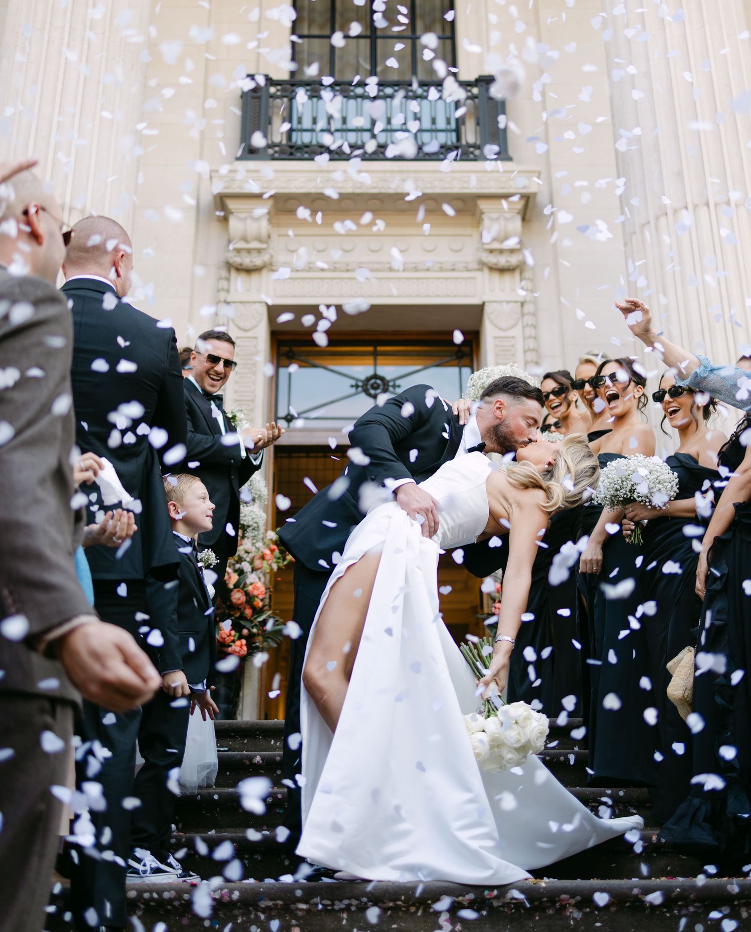 Wedding celebration with confetti being thrown outside a grand building entrance.