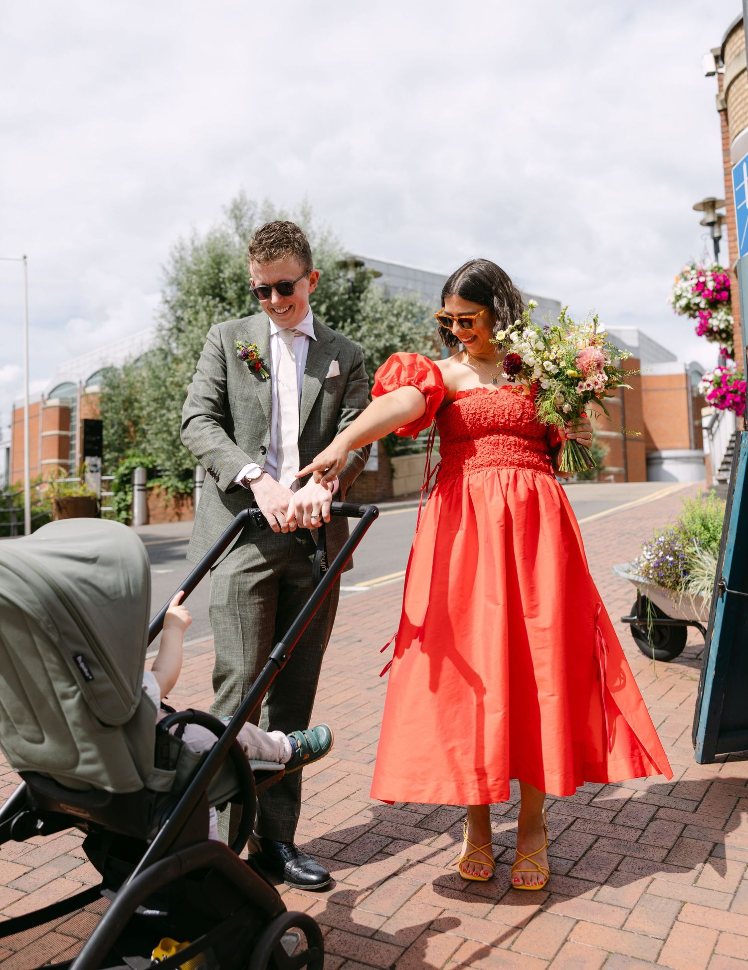 Wedding party members in red dresses and gray suits walk along a brick pathway.