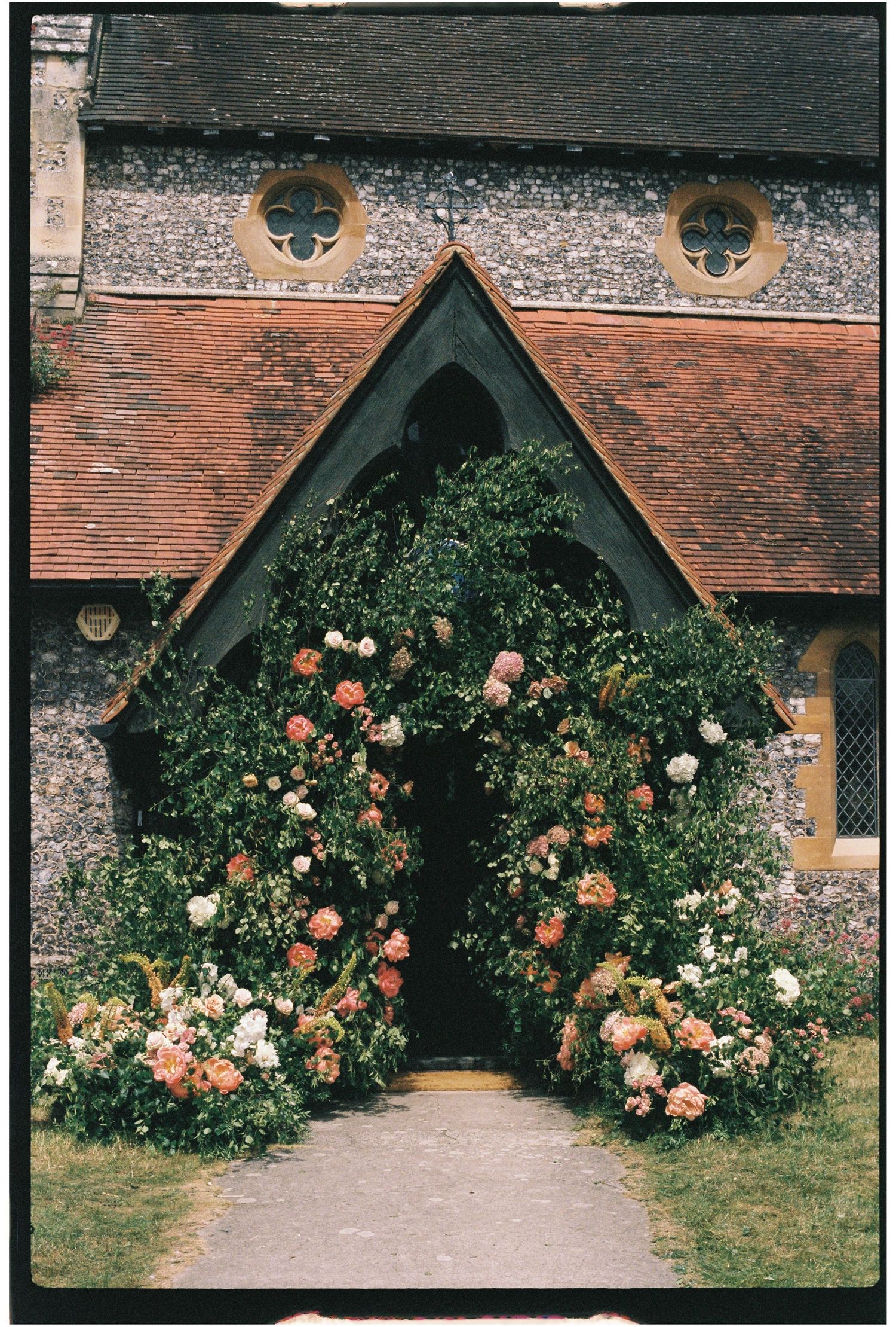 Stunning church entrance adorned with lush floral arch of pink and peach blooms for a wedding.