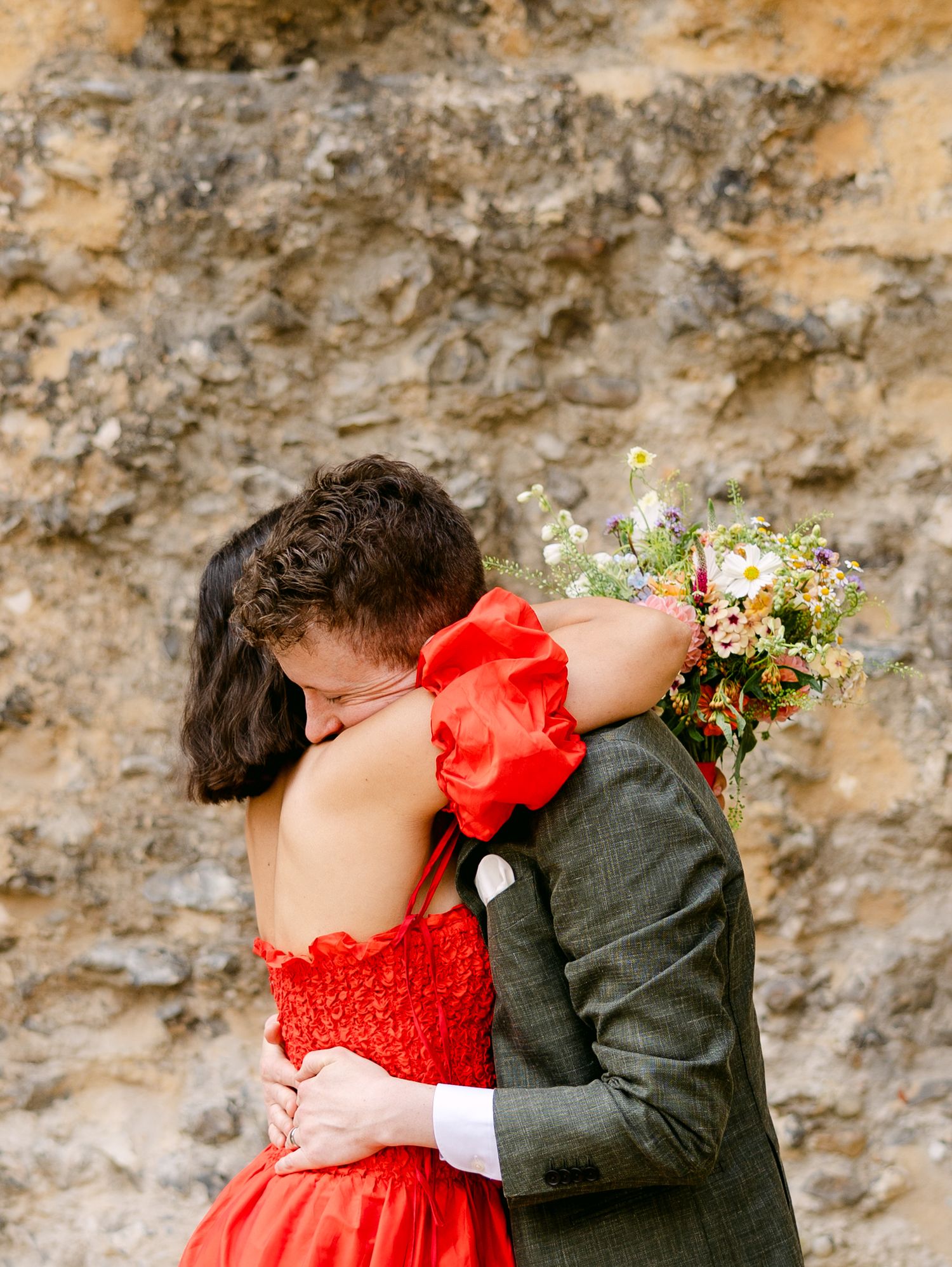 A romantic moment between newlyweds against a stone wall backdrop.
