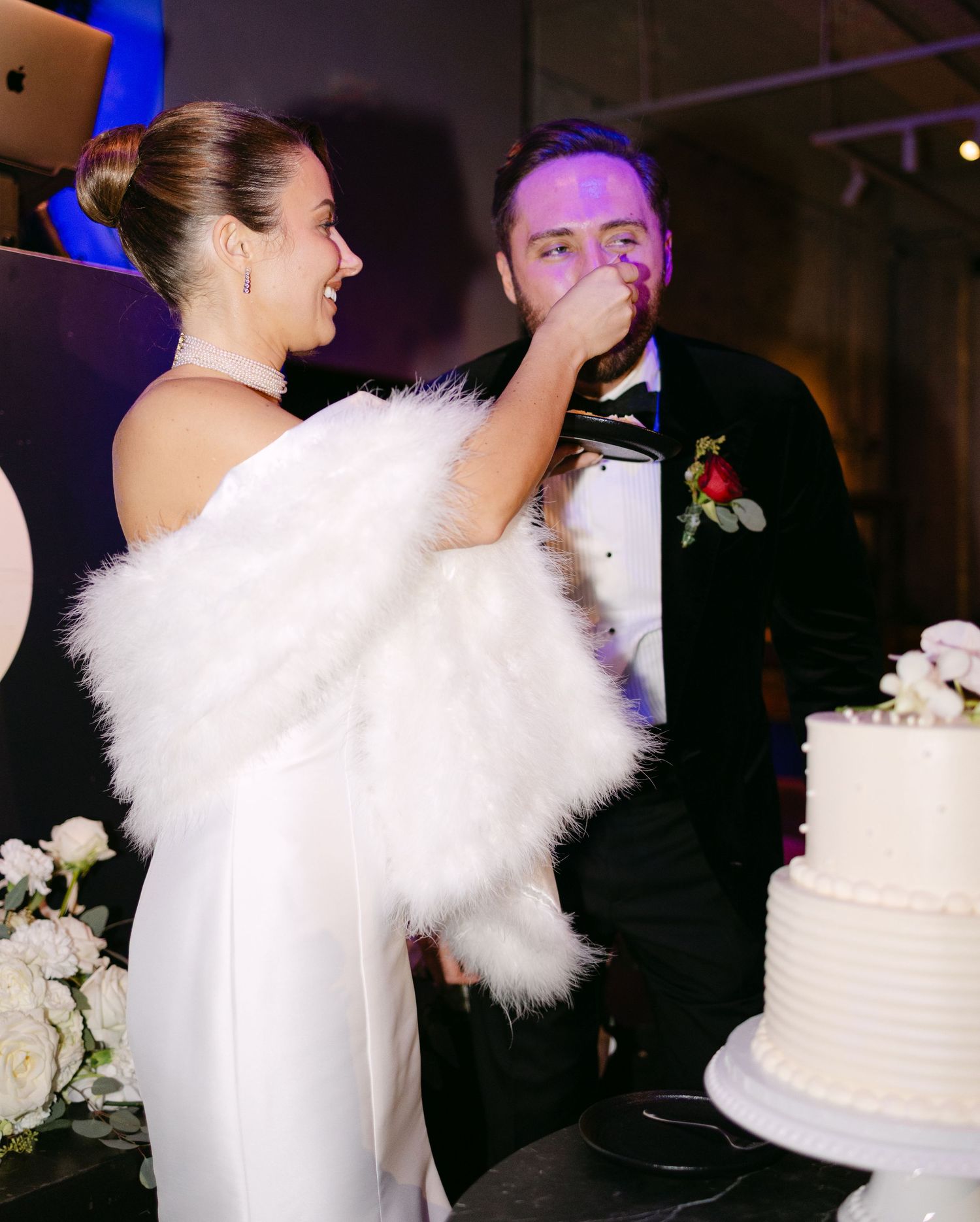 Playful cake cutting moment at wedding reception with bride in white dress and groom in tuxedo.