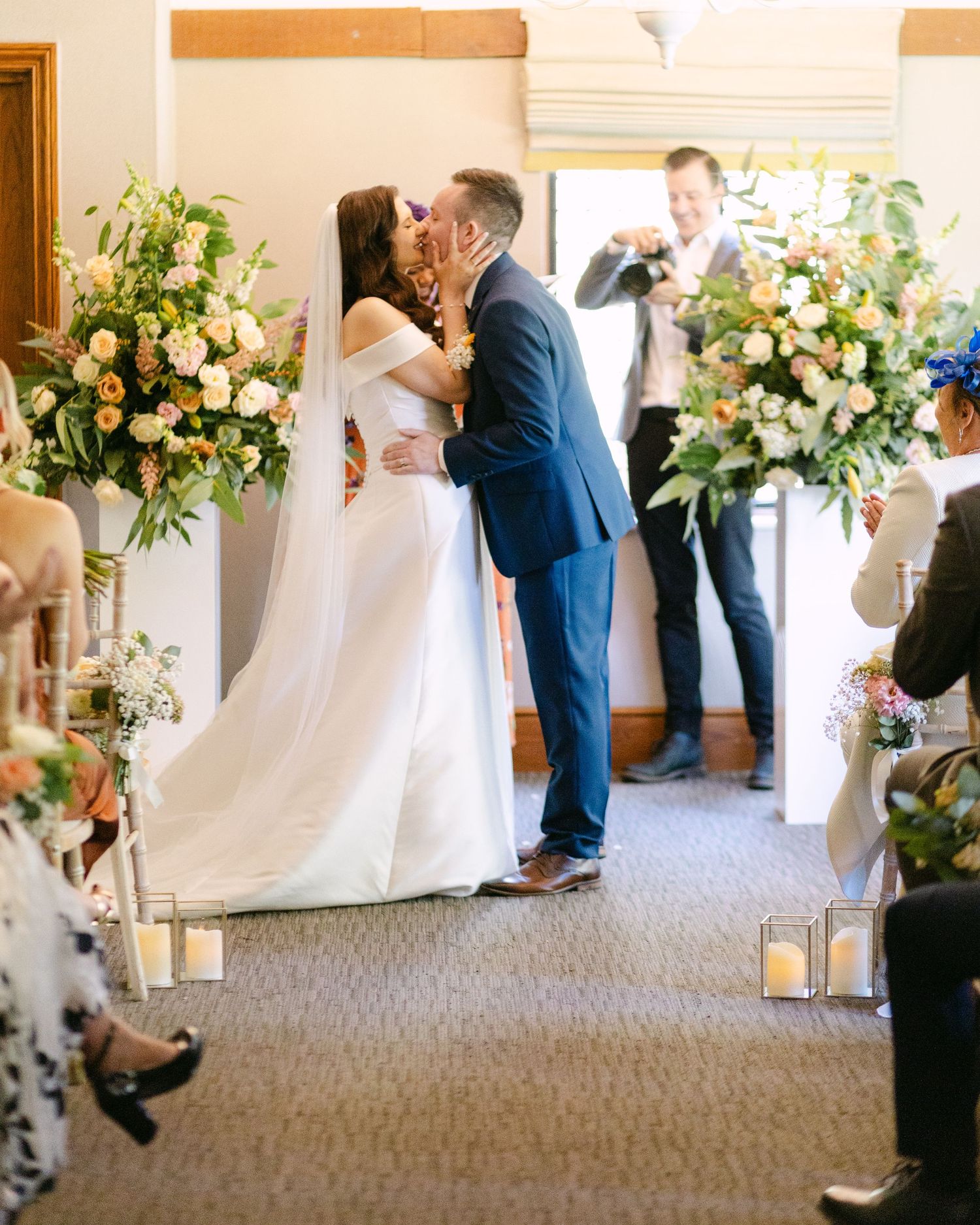 Wedding ceremony space with lantern-lined aisle and white floral arrangements.