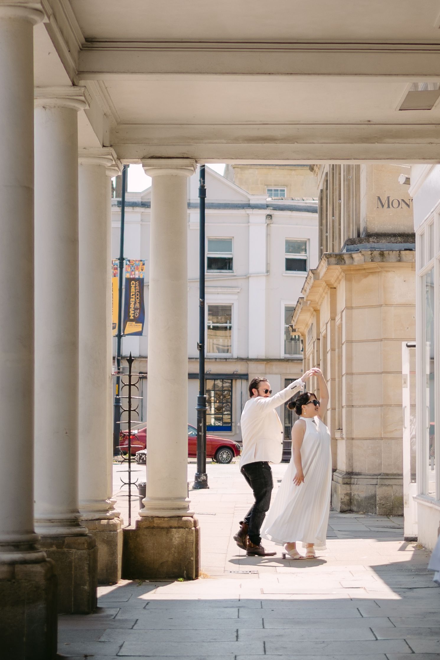 Couple dancing under classical stone columns of a grand building on a sunny urban street.