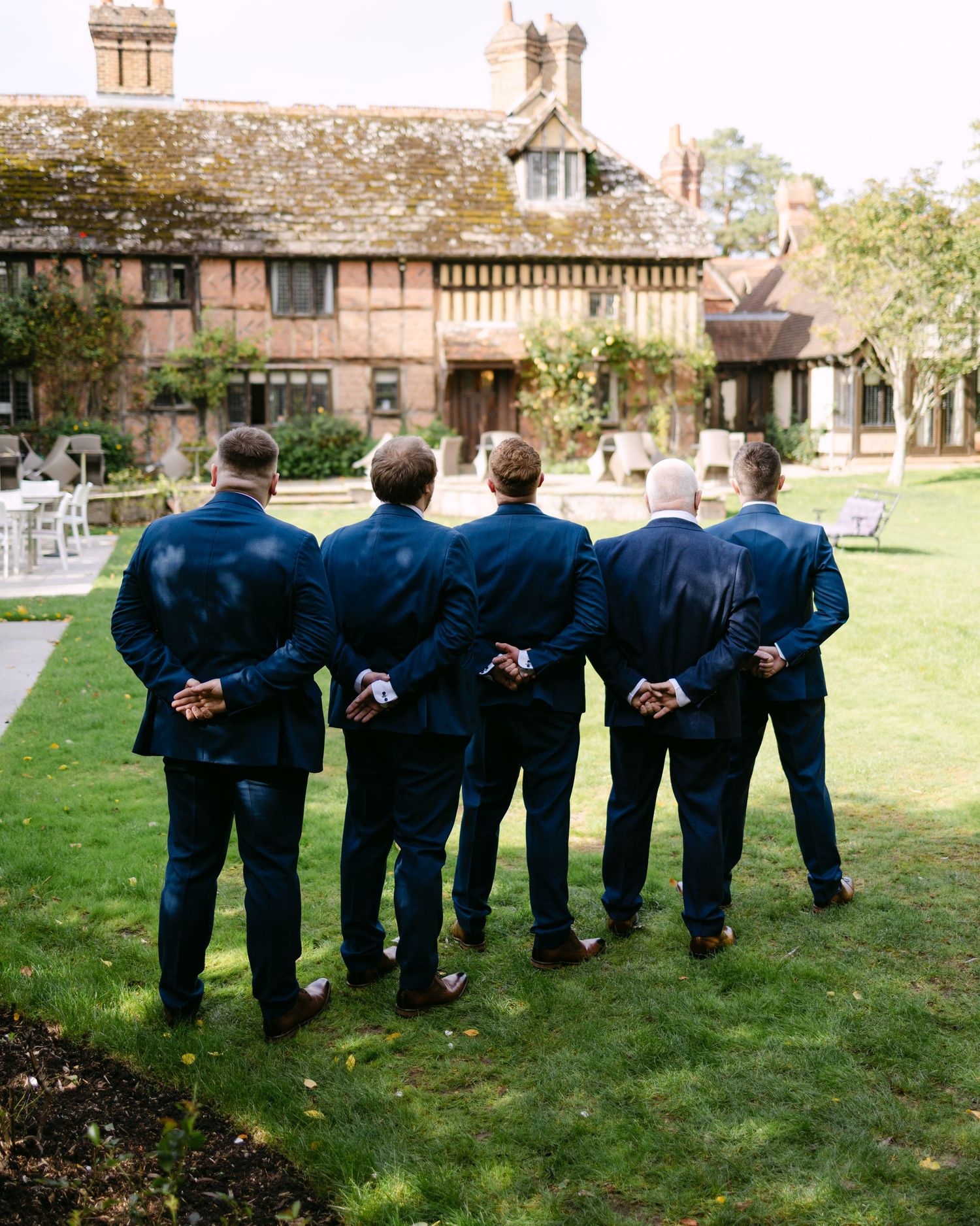 Wedding party in navy suits lined up with hands behind their backs on a grassy lawn.