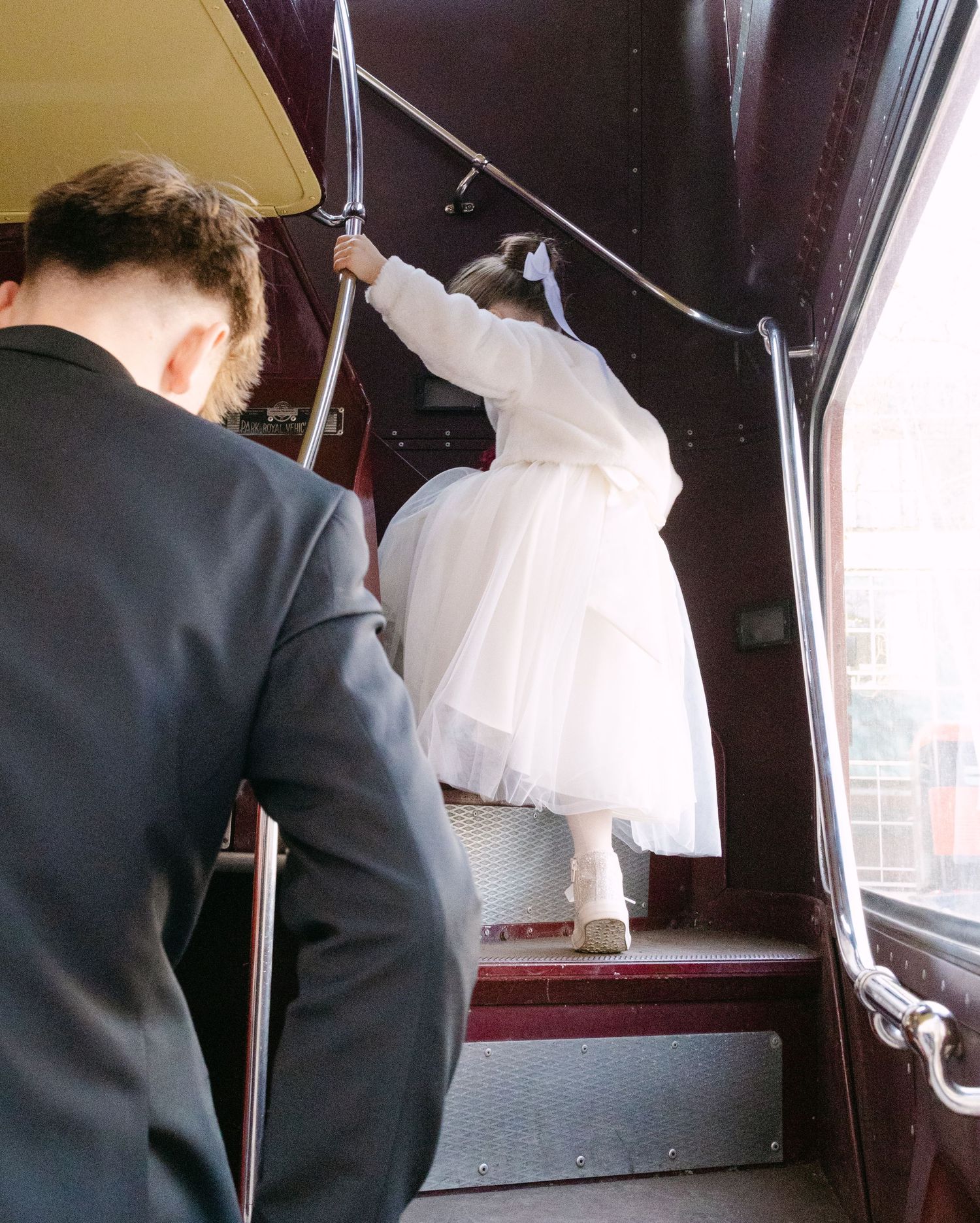 Wedding couple entering vintage vehicle with white dress flowing behind.