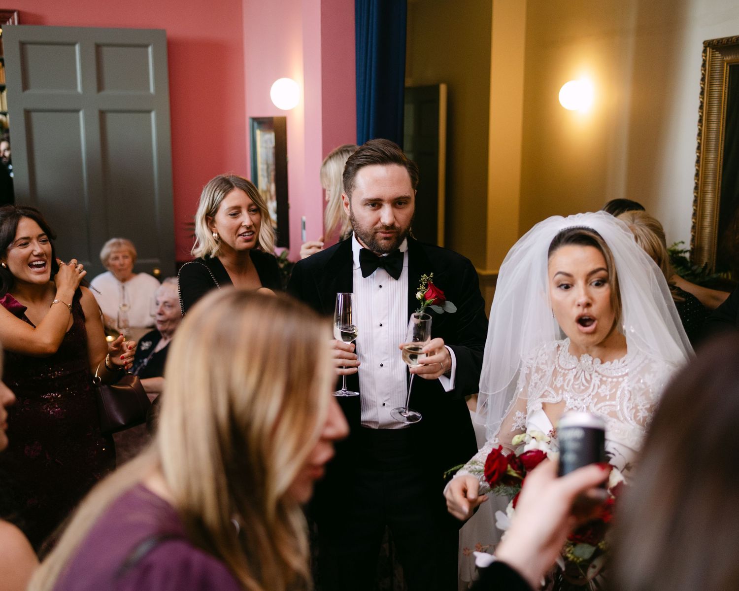 Wedding reception guests enjoying drinks and celebrations in dimly lit venue.