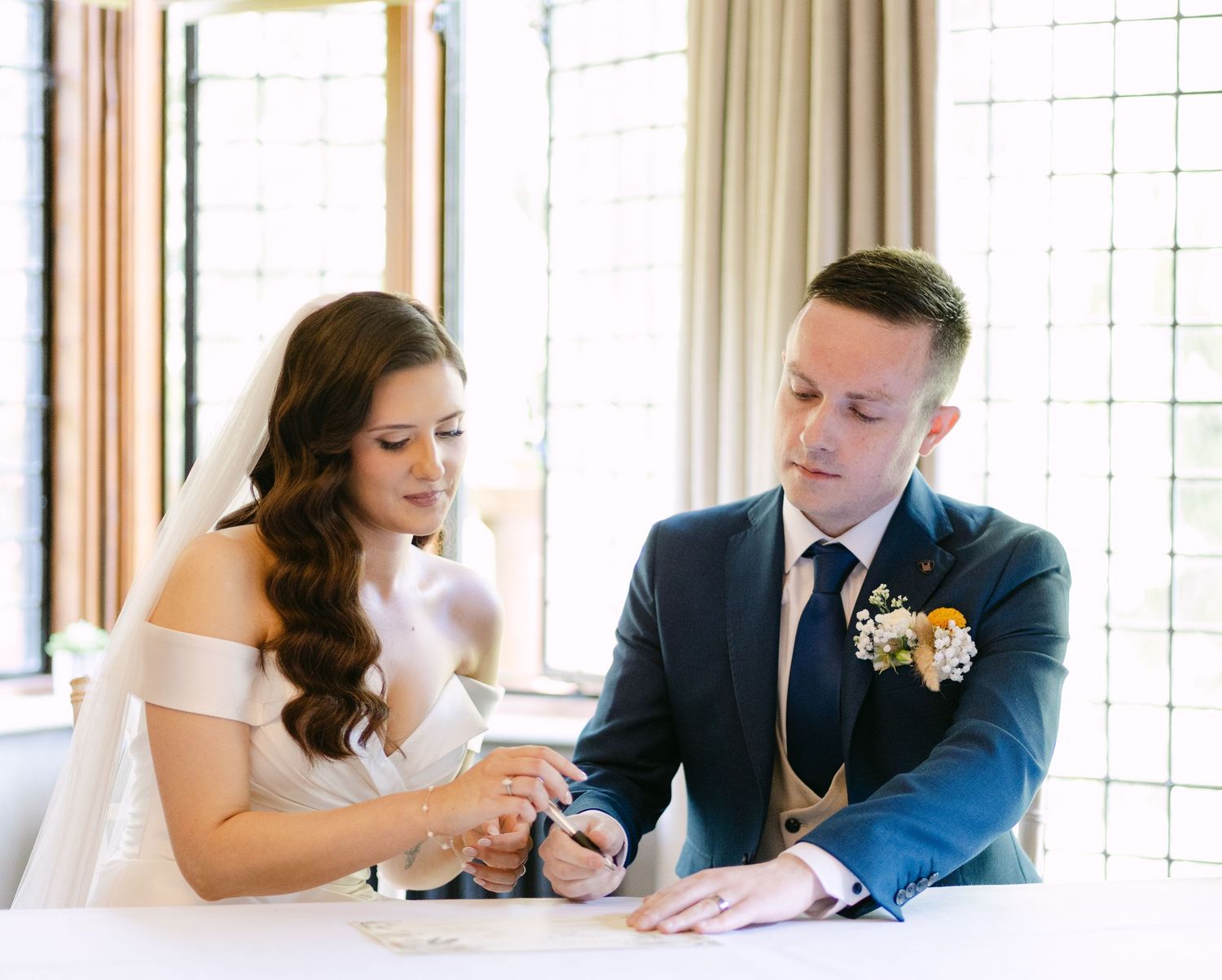 A couple signs documents at a wooden table during a formal ceremony.