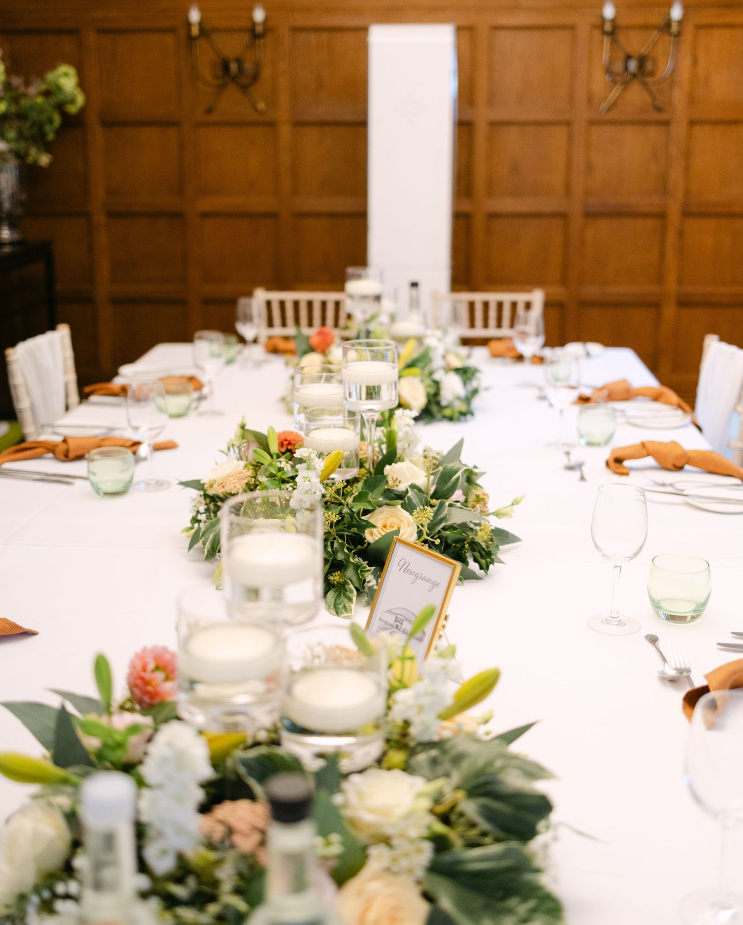 Wedding reception tables decorated with white linens and greenery garlands.