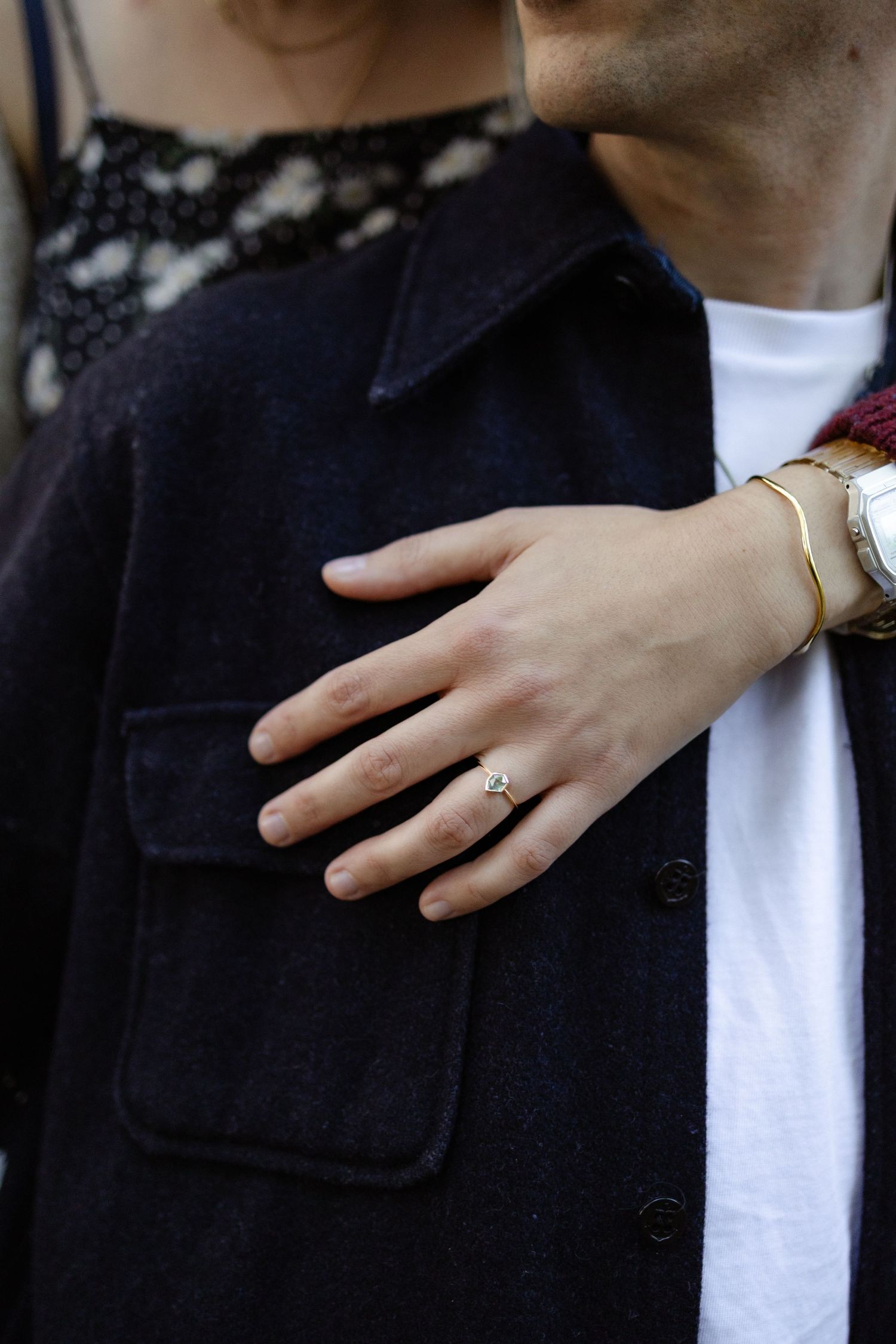 Close-up shots of a hand wearing an engagement ring against a dark jacket.