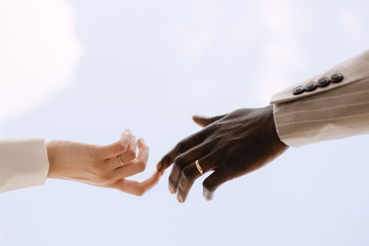Two hands reaching toward each other, one wearing a wedding ring, symbolizing an interracial couple's connection.
