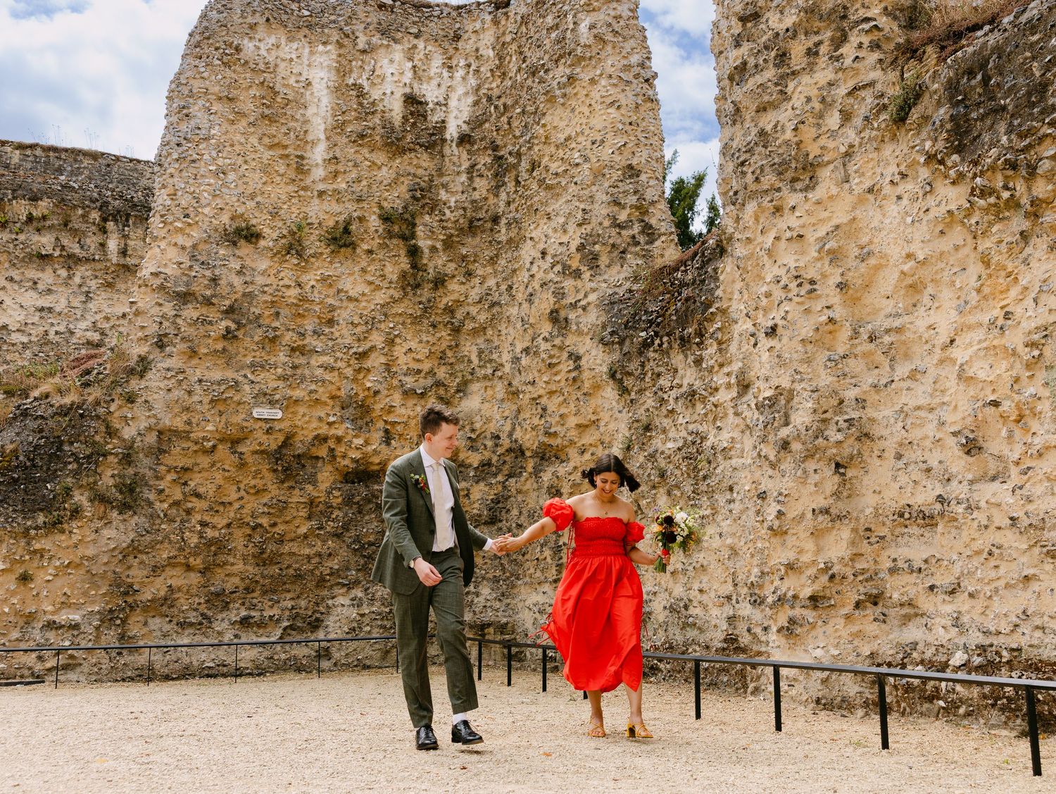 Couple in red dress and suit dancing near ancient stone castle ruins outdoors.