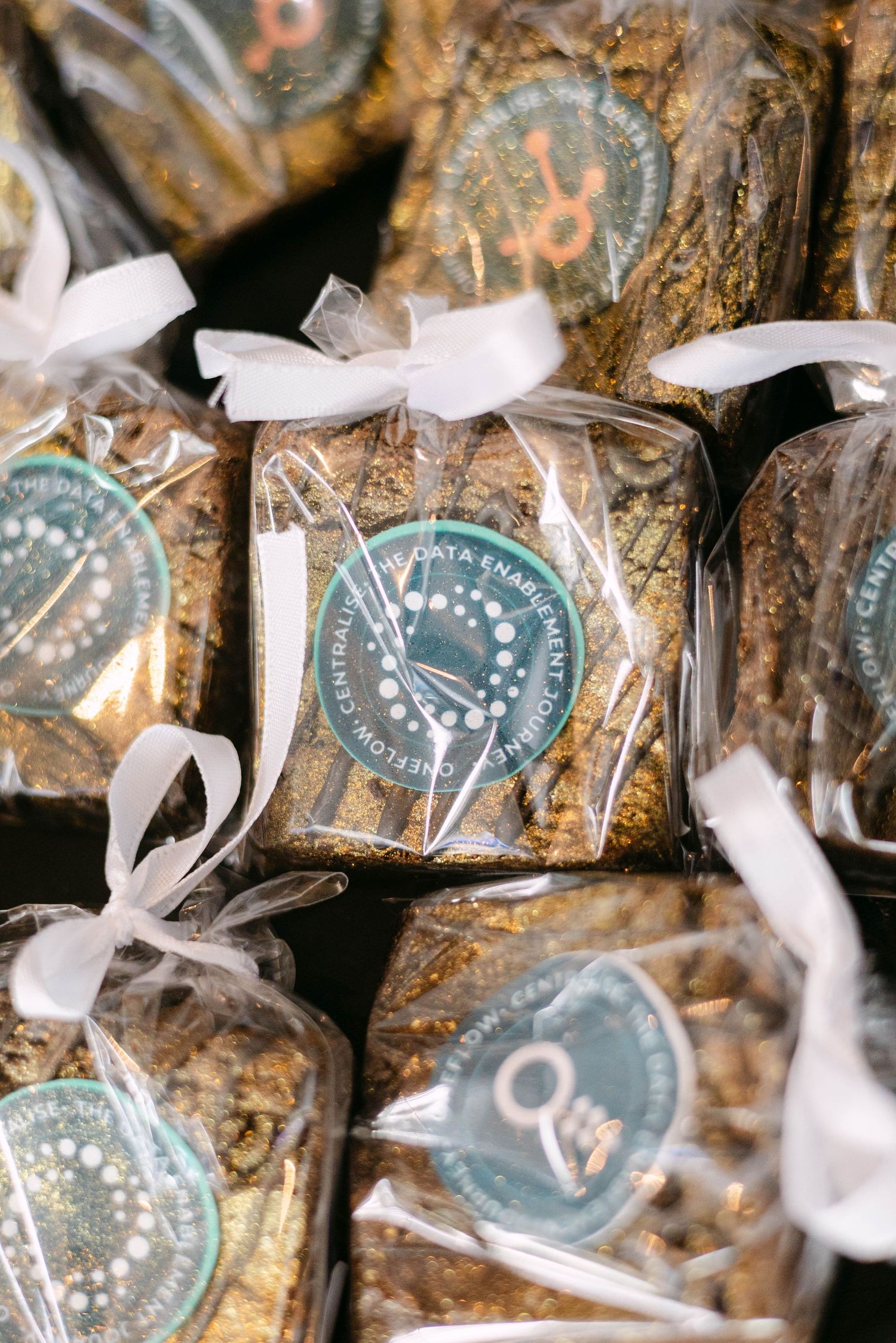 Packaged brownies with teal decorative stickers and white ribbon bows, presented as elegant gift favors.