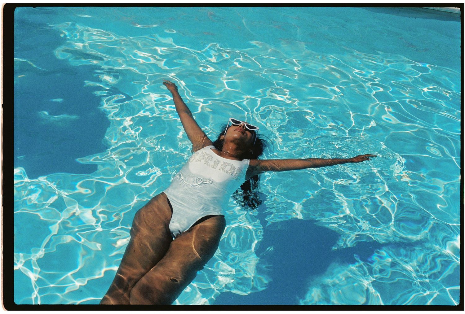 Aerial color photo of a woman in a white swimsuit floating peacefully in a bright blue pool.