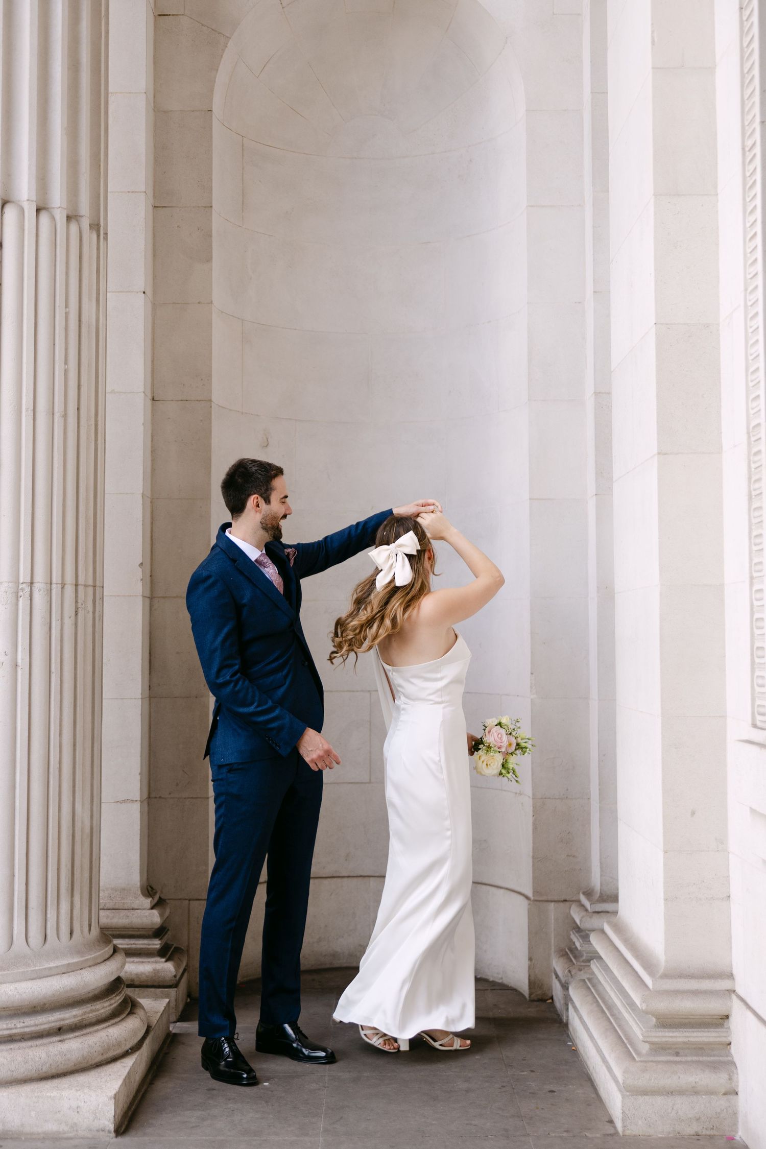 A couple in wedding attire dances between elegant white columns in a romantic way at The Old Marylebone Town Hall.