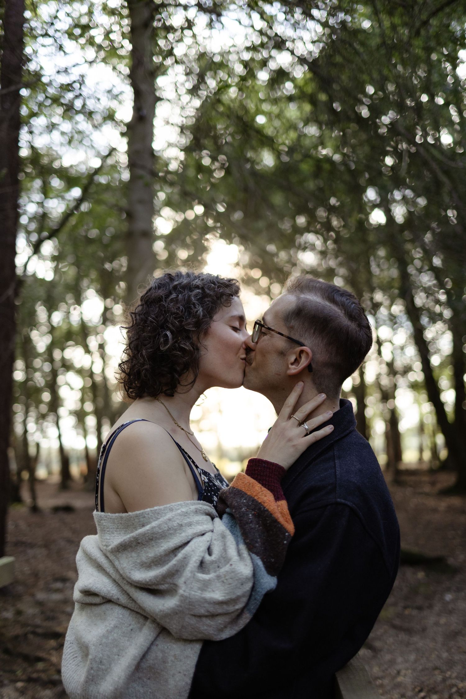 An intimate moment shared between a couple in a wooded setting with sunlight filtering through trees.