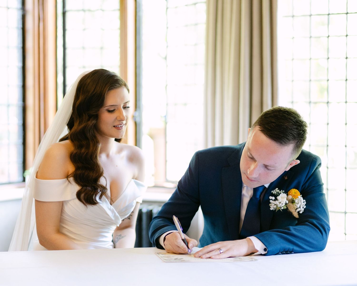 A couple signs documents at a wooden table during a formal ceremony.