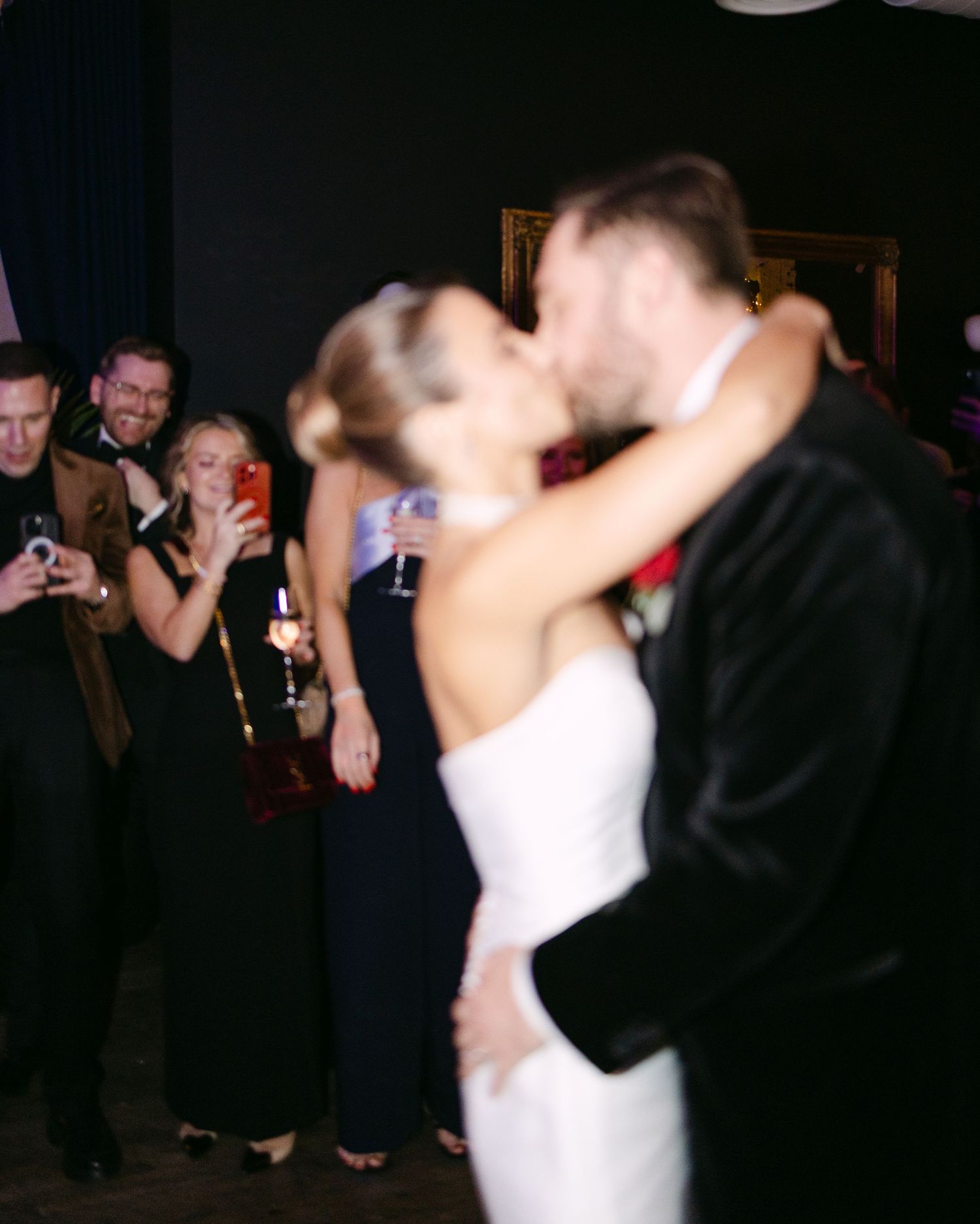 Newlyweds share romantic first dance while wedding guests watch and take photos.