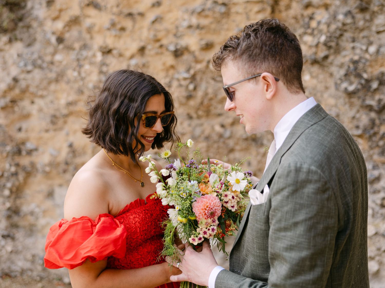 Couple shares an intimate moment during their wedding photoshoot by a textured stone wall.
